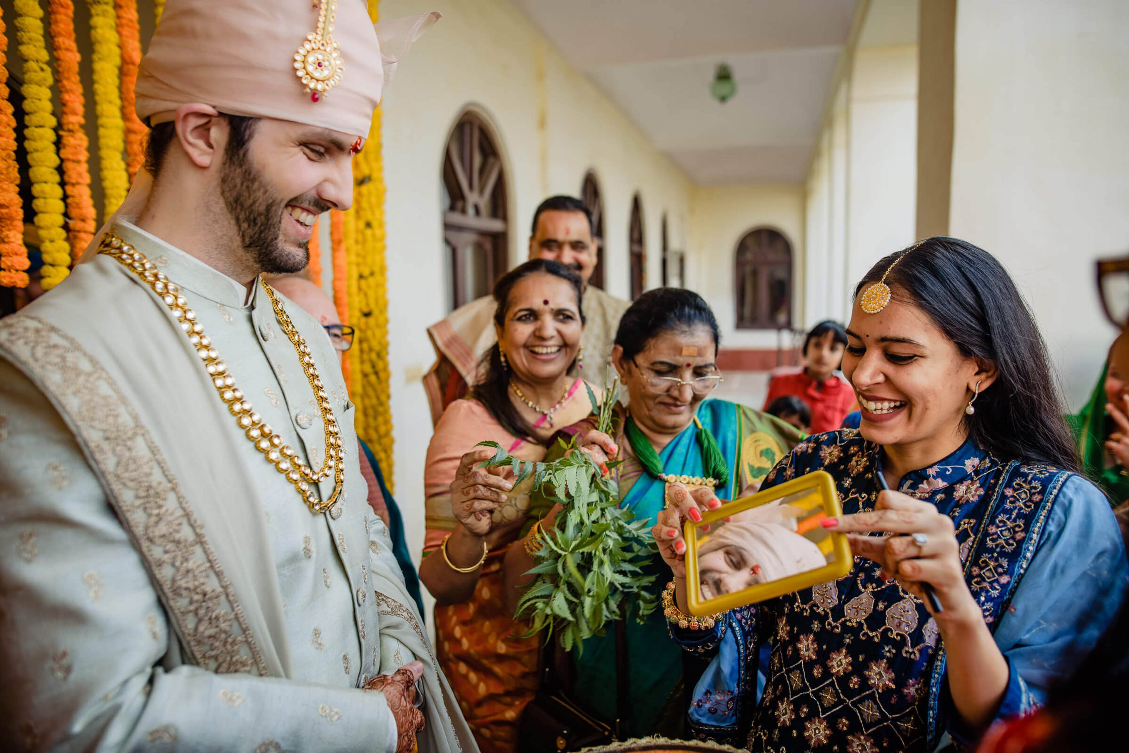 Groom Eric in traditional white sherwani and turban laughing with family holding gifts in Rajasthan