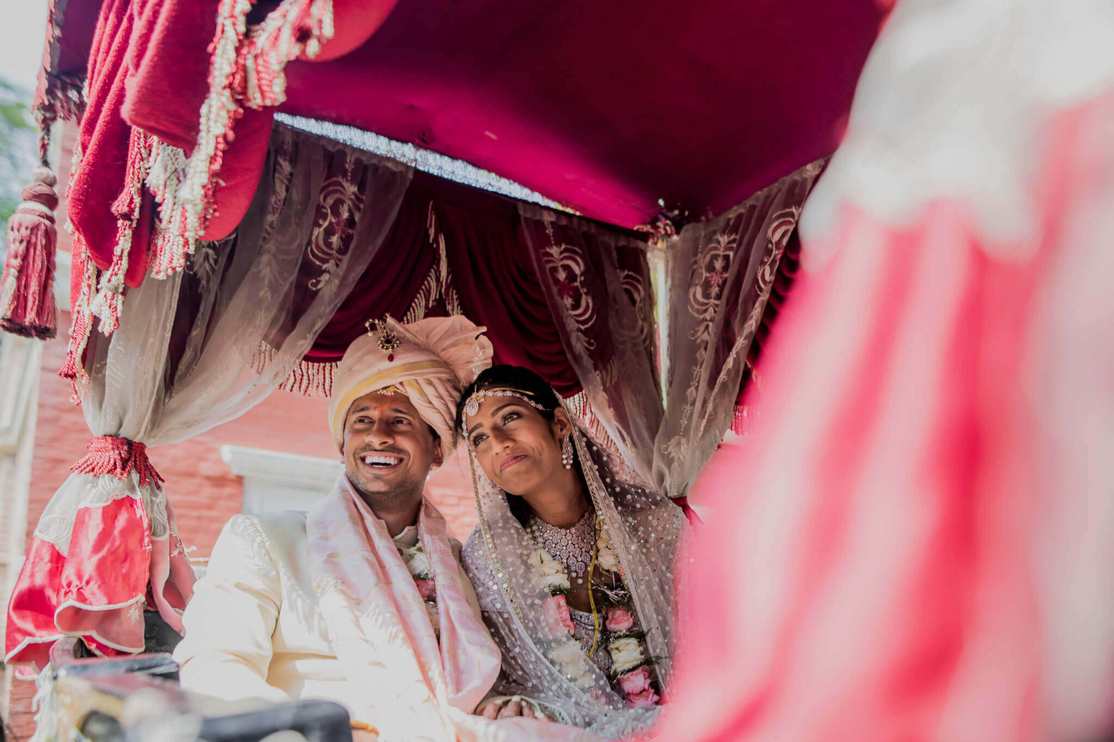 Anu and Raghu smile together beneath a vibrant pink ceremonial canopy in Nepal