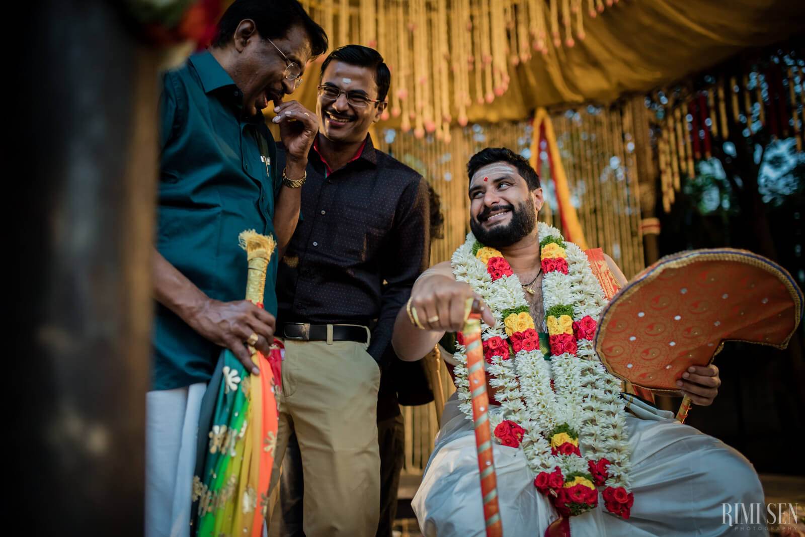 Three men in traditional Indian attire celebrate at Bangalore wedding under golden fabric backdrop