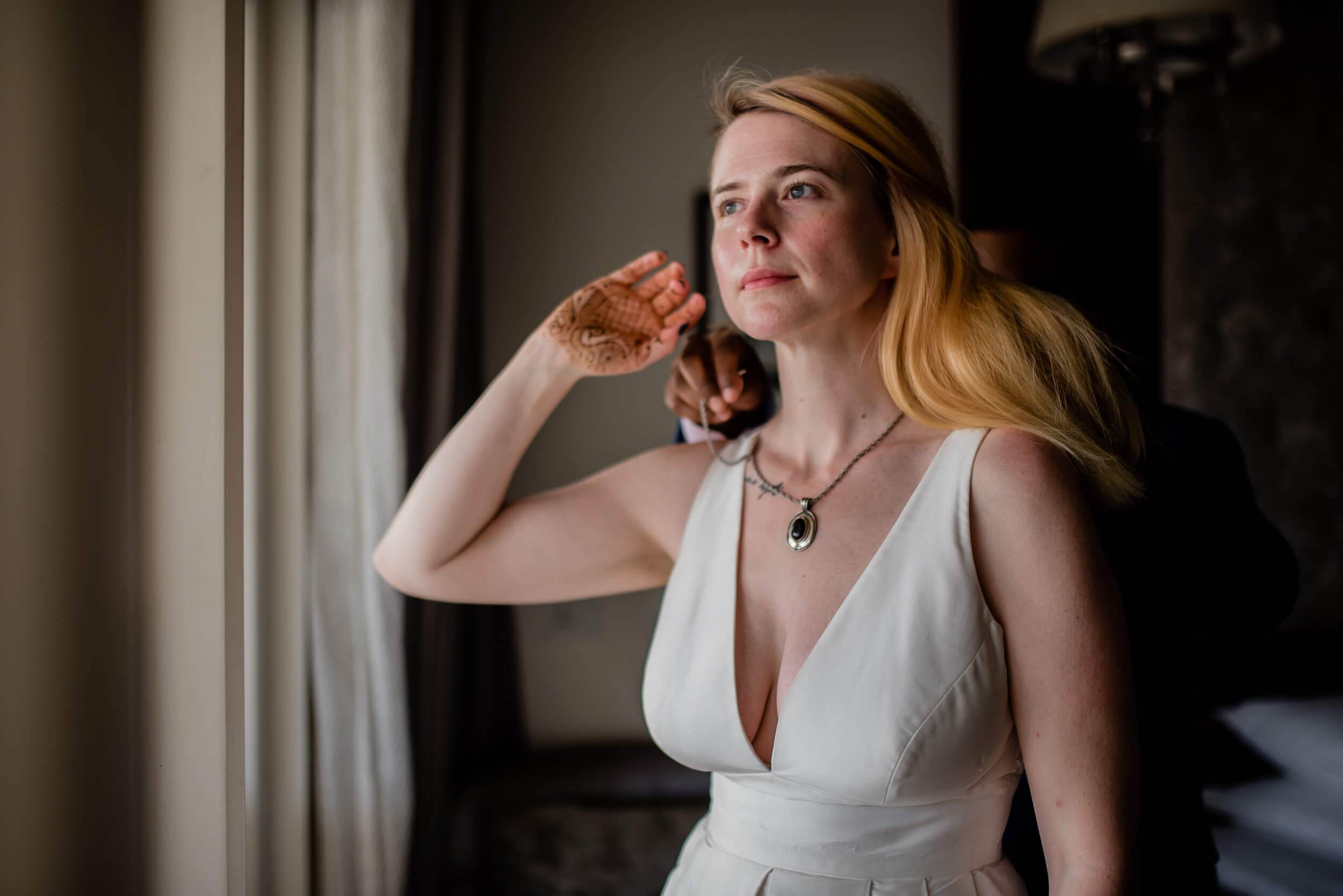 Sarah in white draped dress gazes thoughtfully by window in Goa