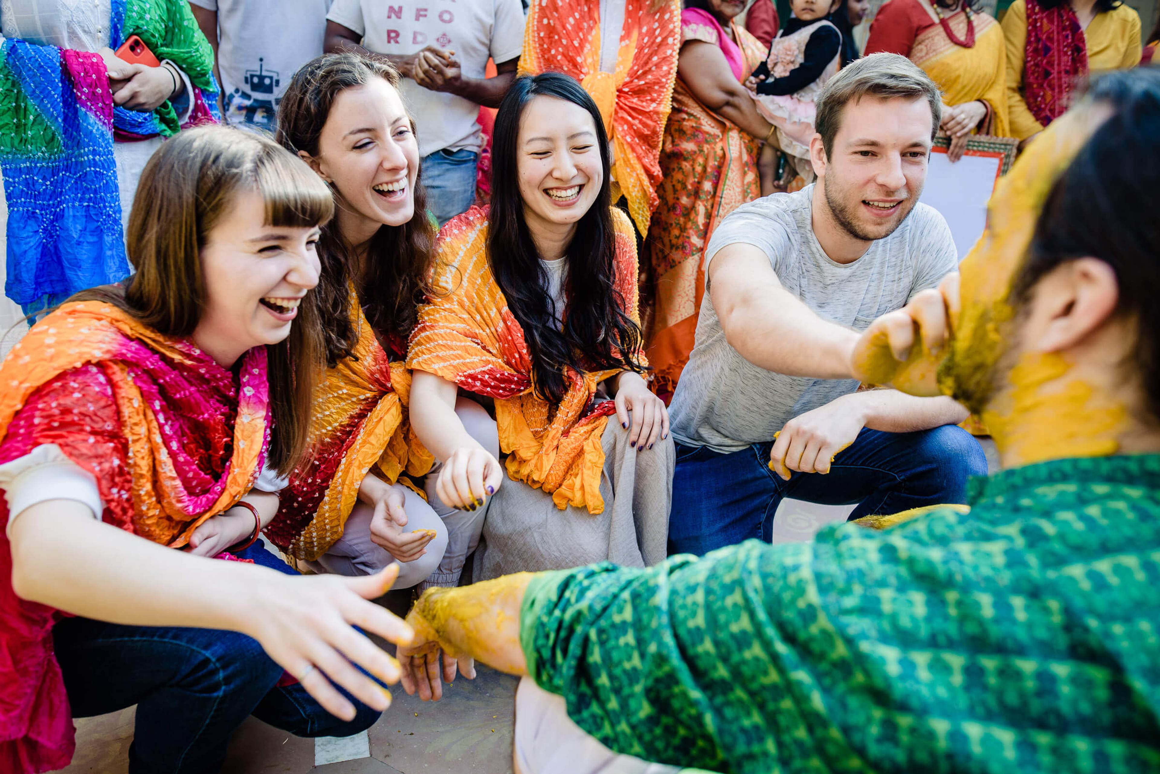Maitrayee and Eric laugh with friends wearing colorful traditional fabrics in Rajasthan market setting
