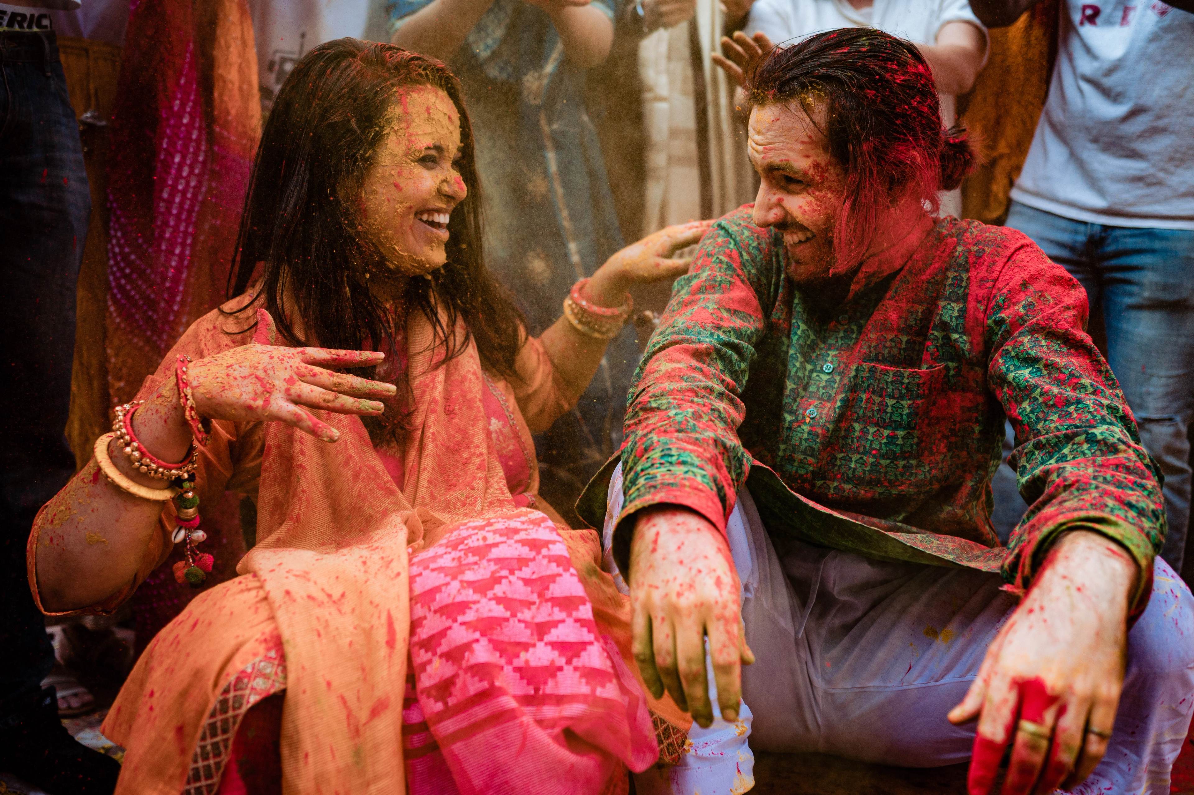 Couple laughing together covered in colored powder during Holi celebration, wearing traditional festive attire