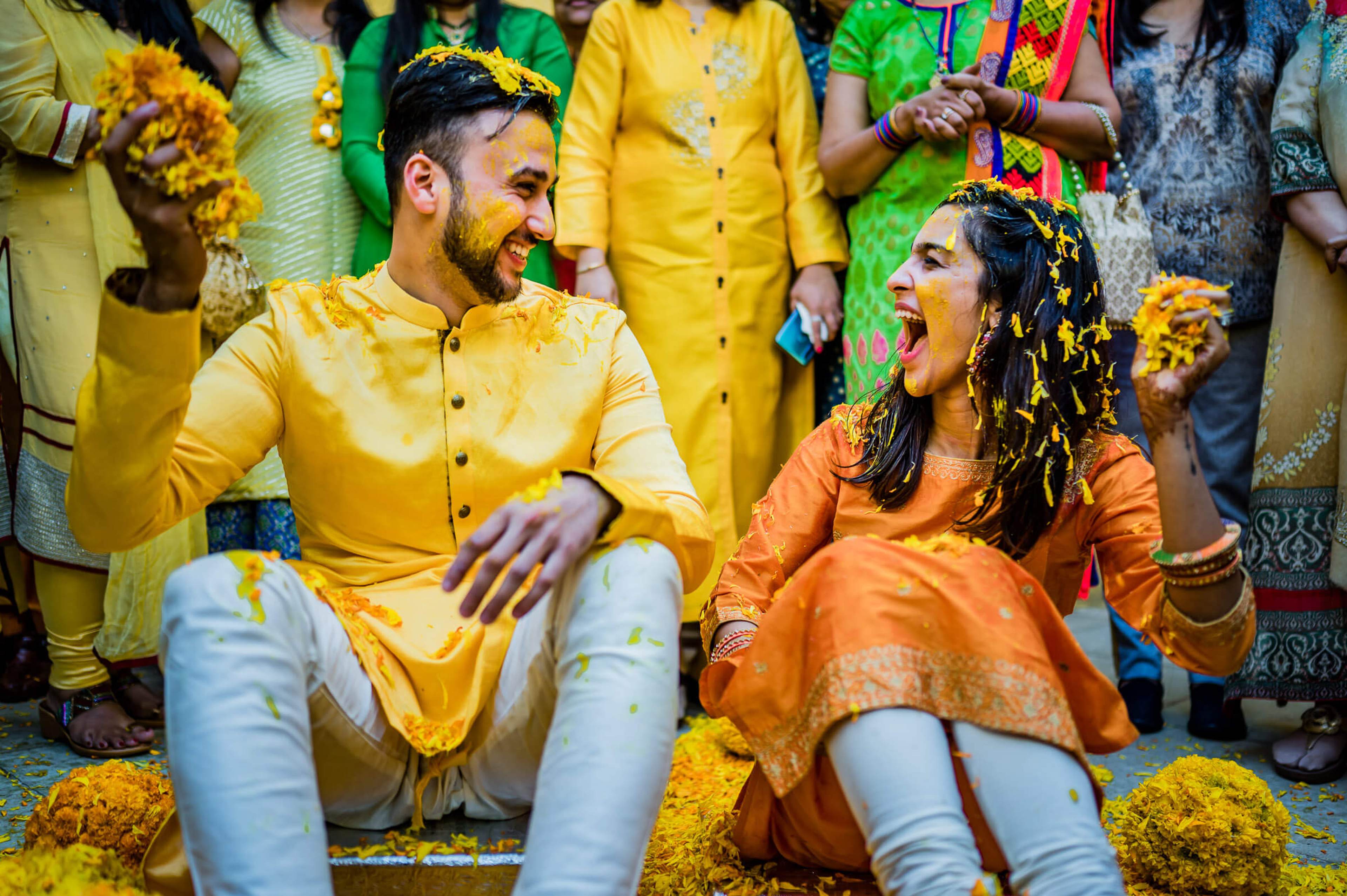 Shreya and Yash laugh together covered in yellow turmeric powder during Haldi celebration in Mahabaleshwar, surrounded by joyful guests
