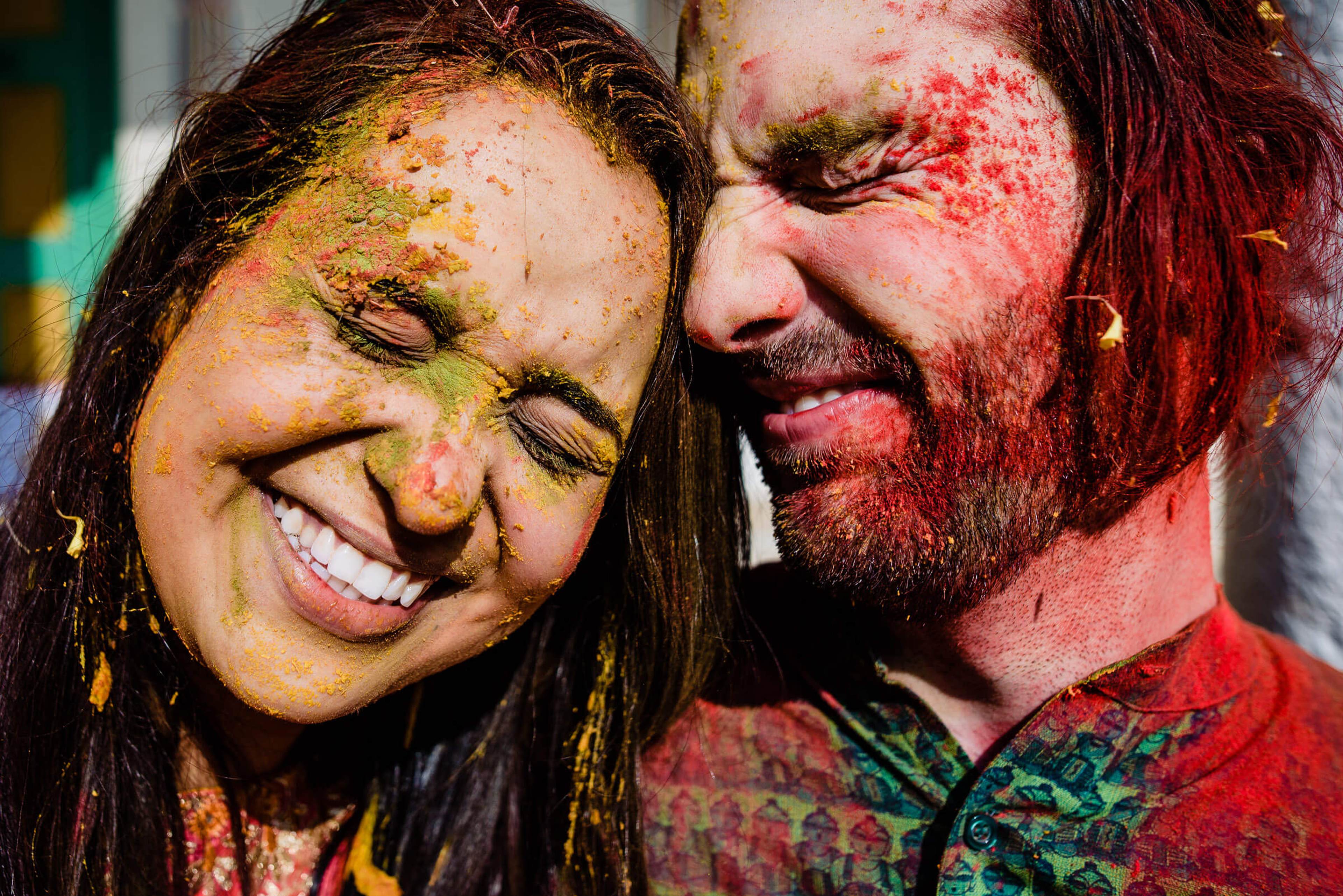 Maitrayee and Eric smile together, faces covered in vibrant Holi powder paint in Rajasthan