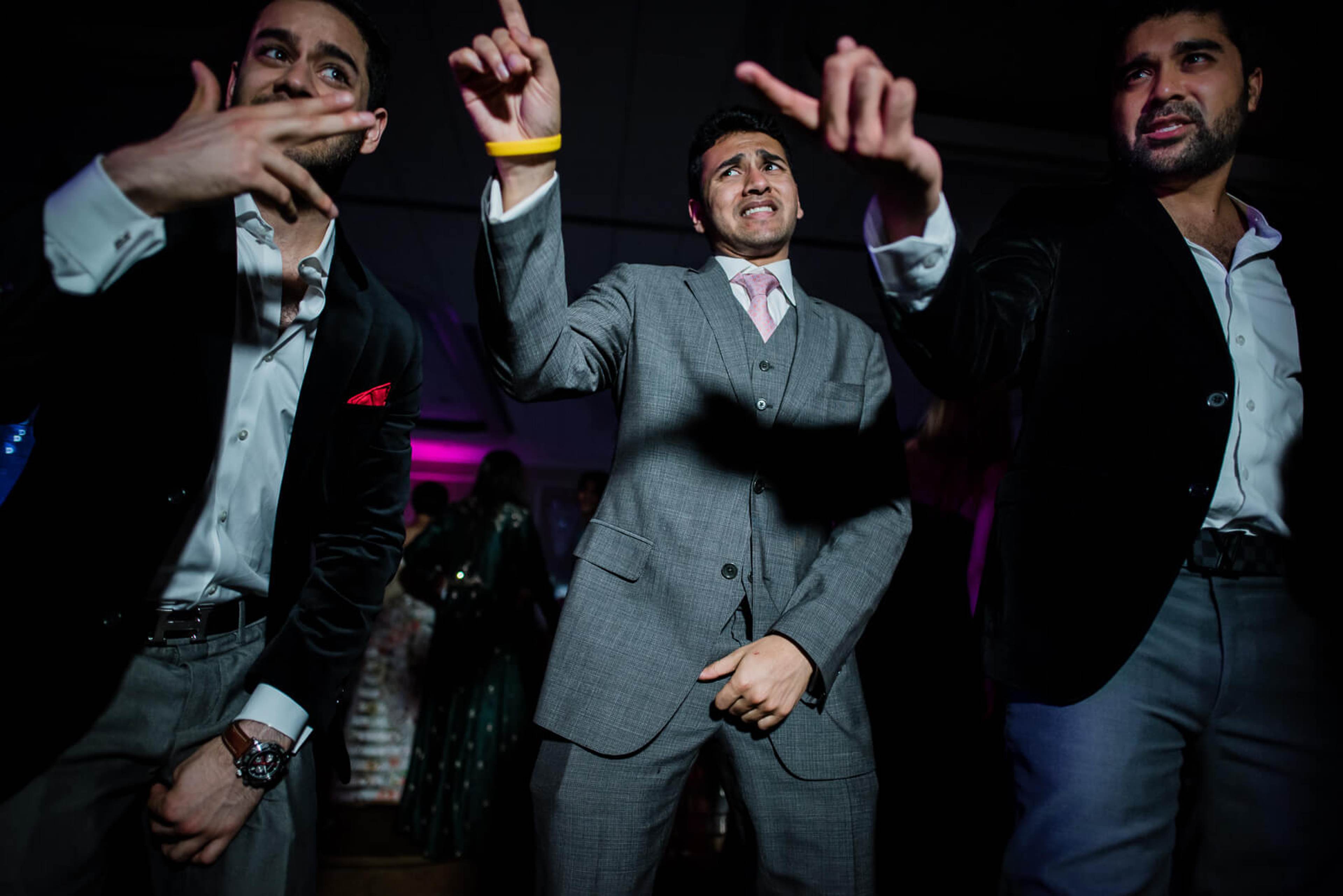 Ankit and groomsmen dancing energetically in suits under colorful stage lighting at New York reception