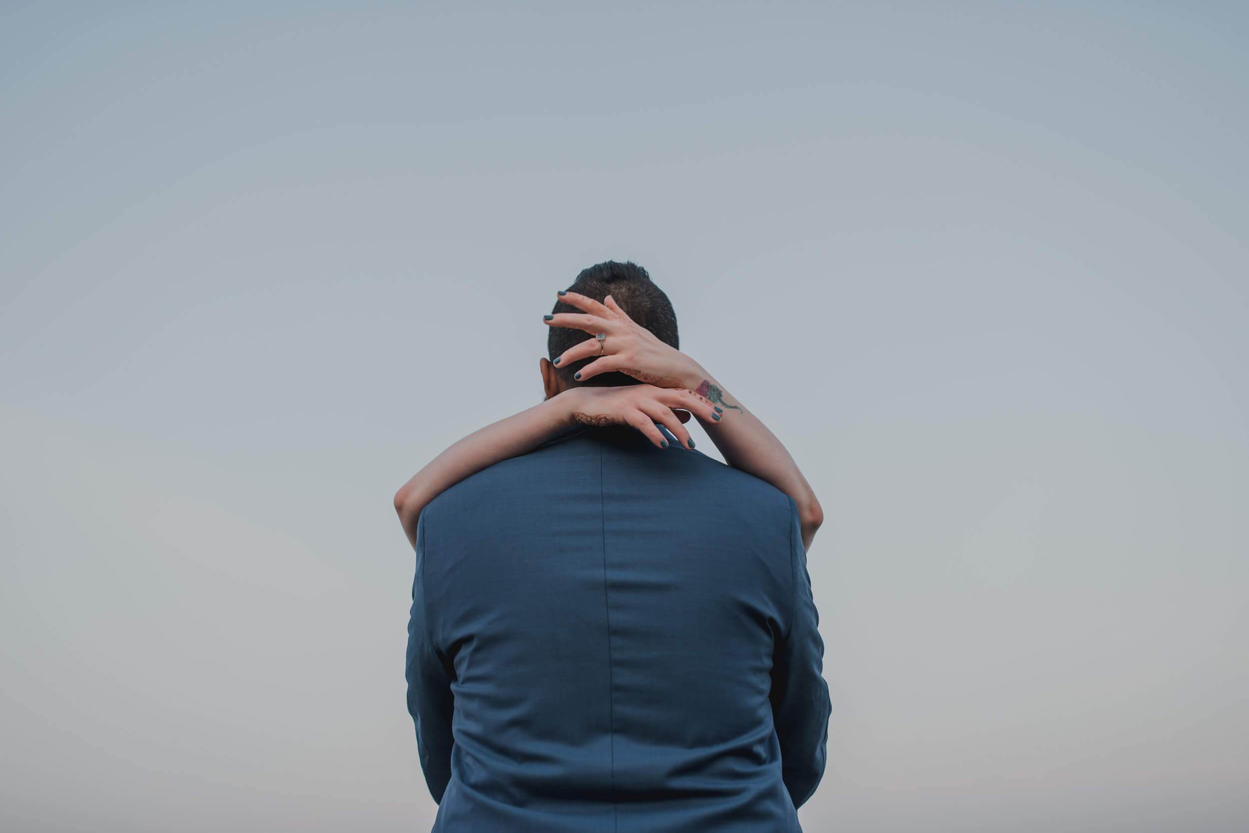 Sarah and Ravin embrace against clear sky, shot from behind in Goa