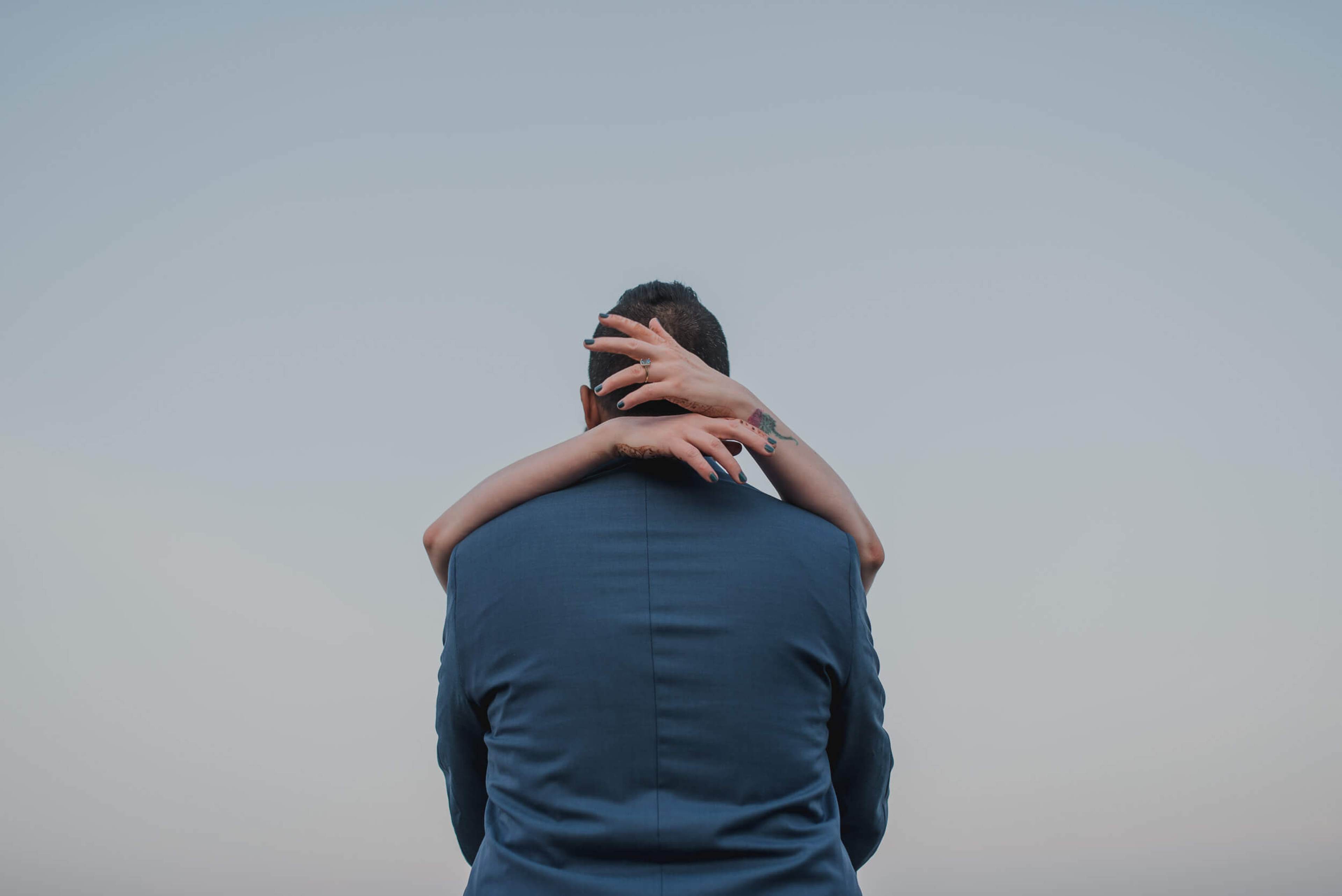 Sarah and Ravin embrace against clear sky, shot from behind in Goa