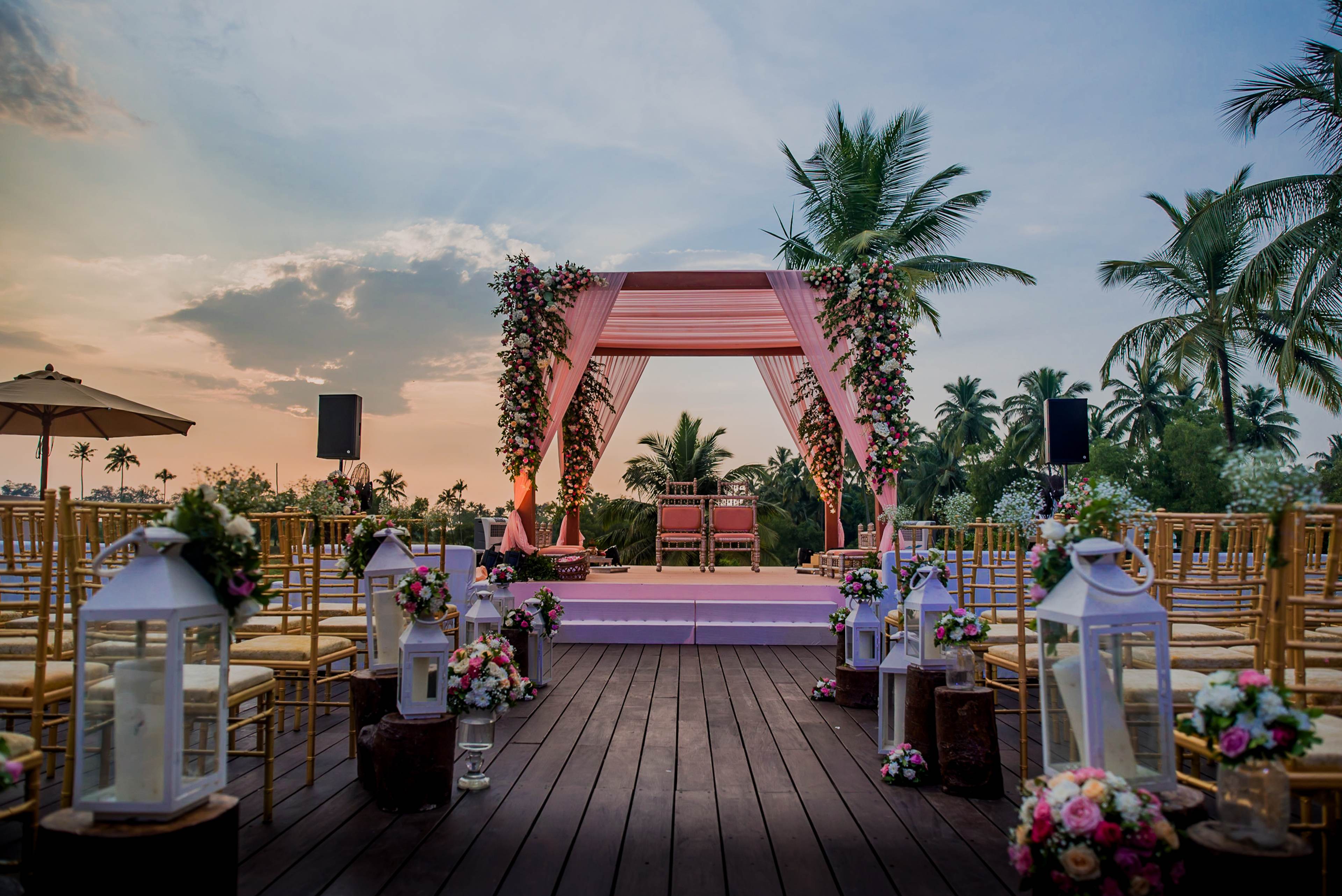 Avani & Srikant's pink wedding arch with floral arrangements and palm trees at sunset in Goa