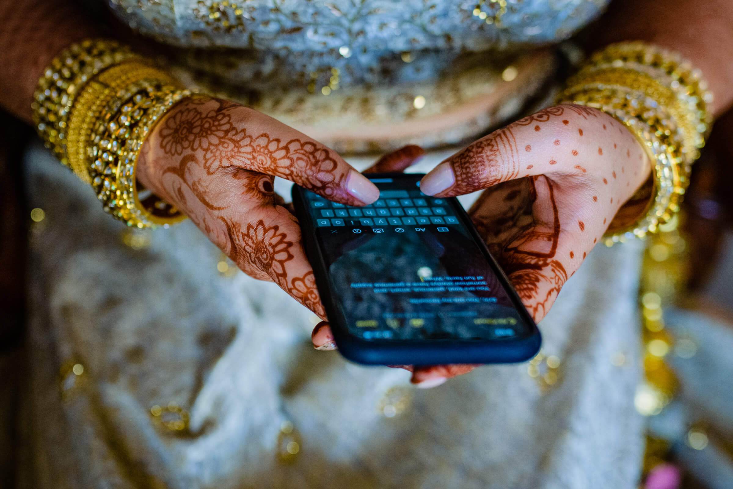 Maitrayee and Eric's hands with henna and gold bangles holding a phone in Rajasthan