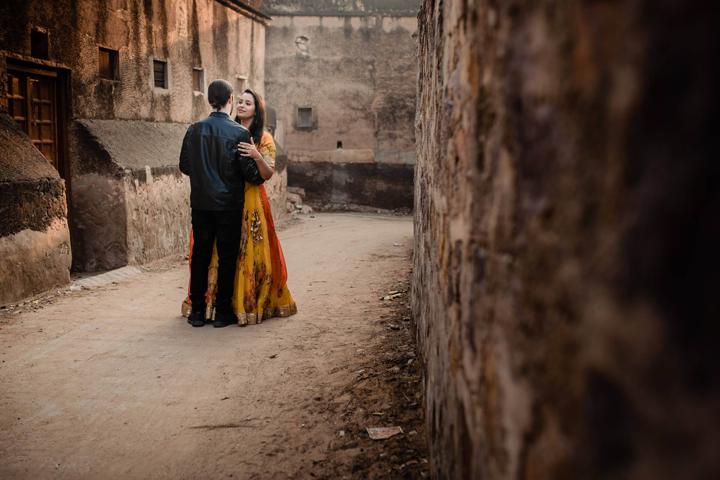 Maitrayee and Eric embrace in a narrow alleyway framed by weathered stone walls in Rajasthan
