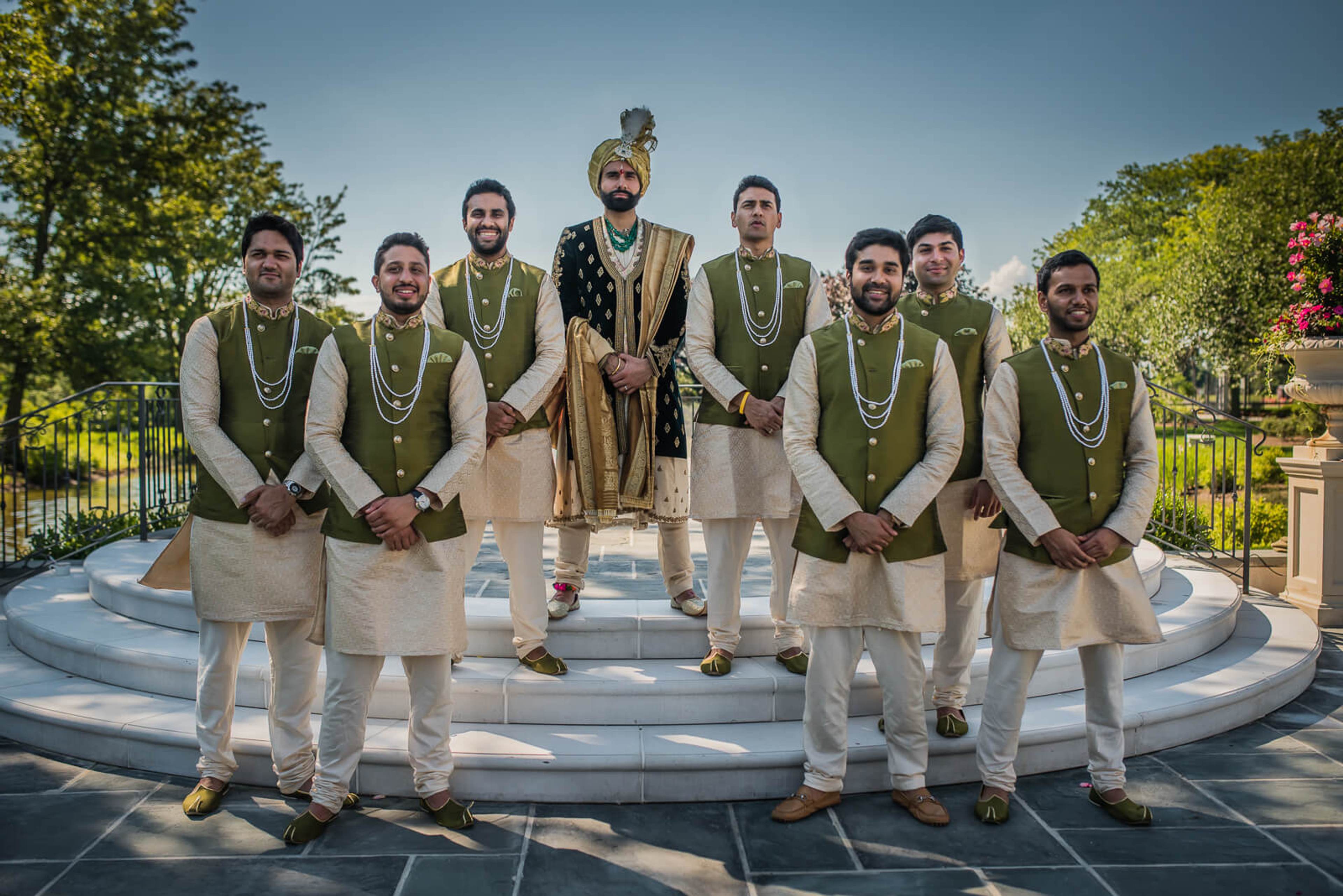 Groom and groomsmen in traditional Indian attire with green vests and garlands on circular stone platform, New York