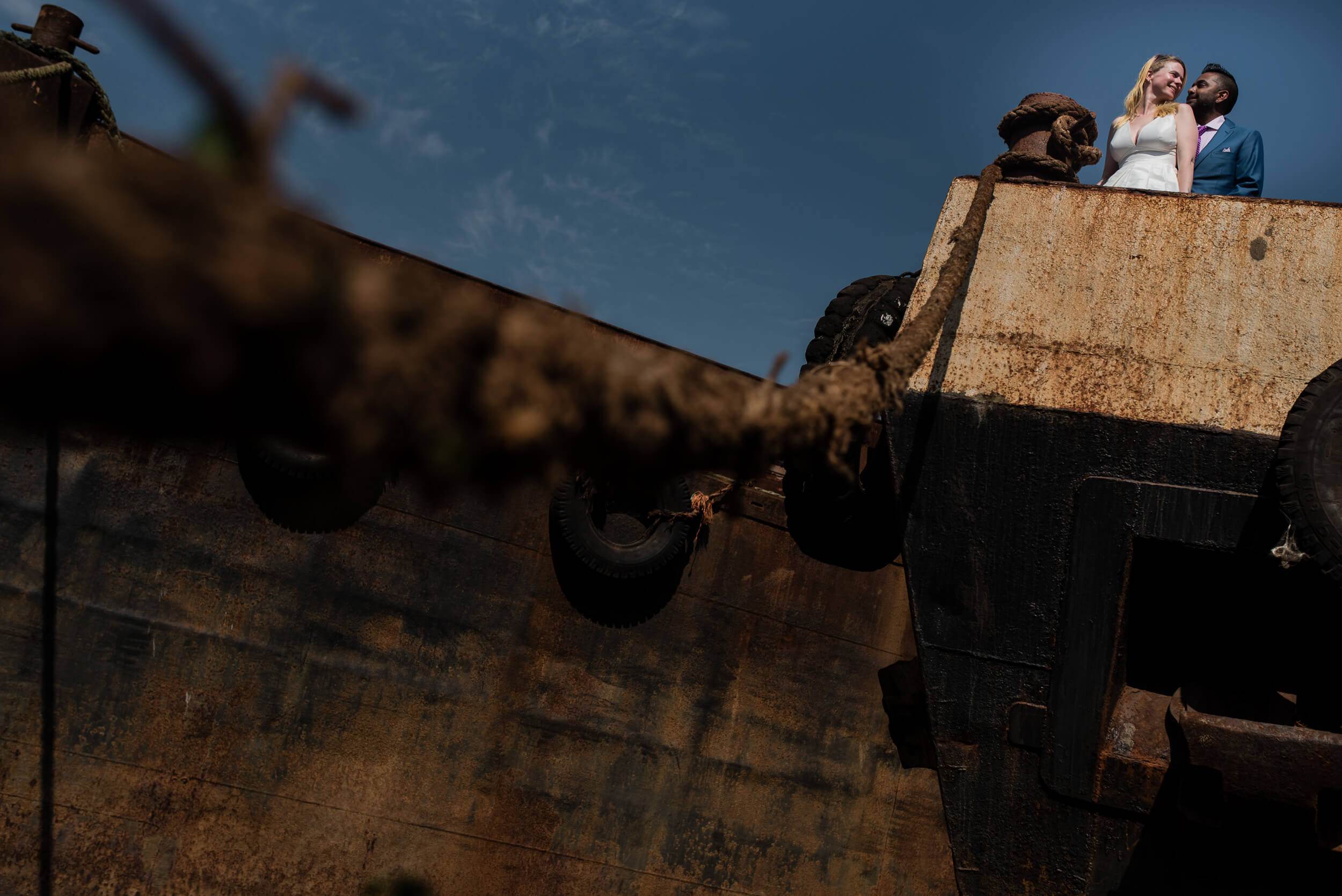 Couple stands on rusty industrial structure against blue sky in Goa