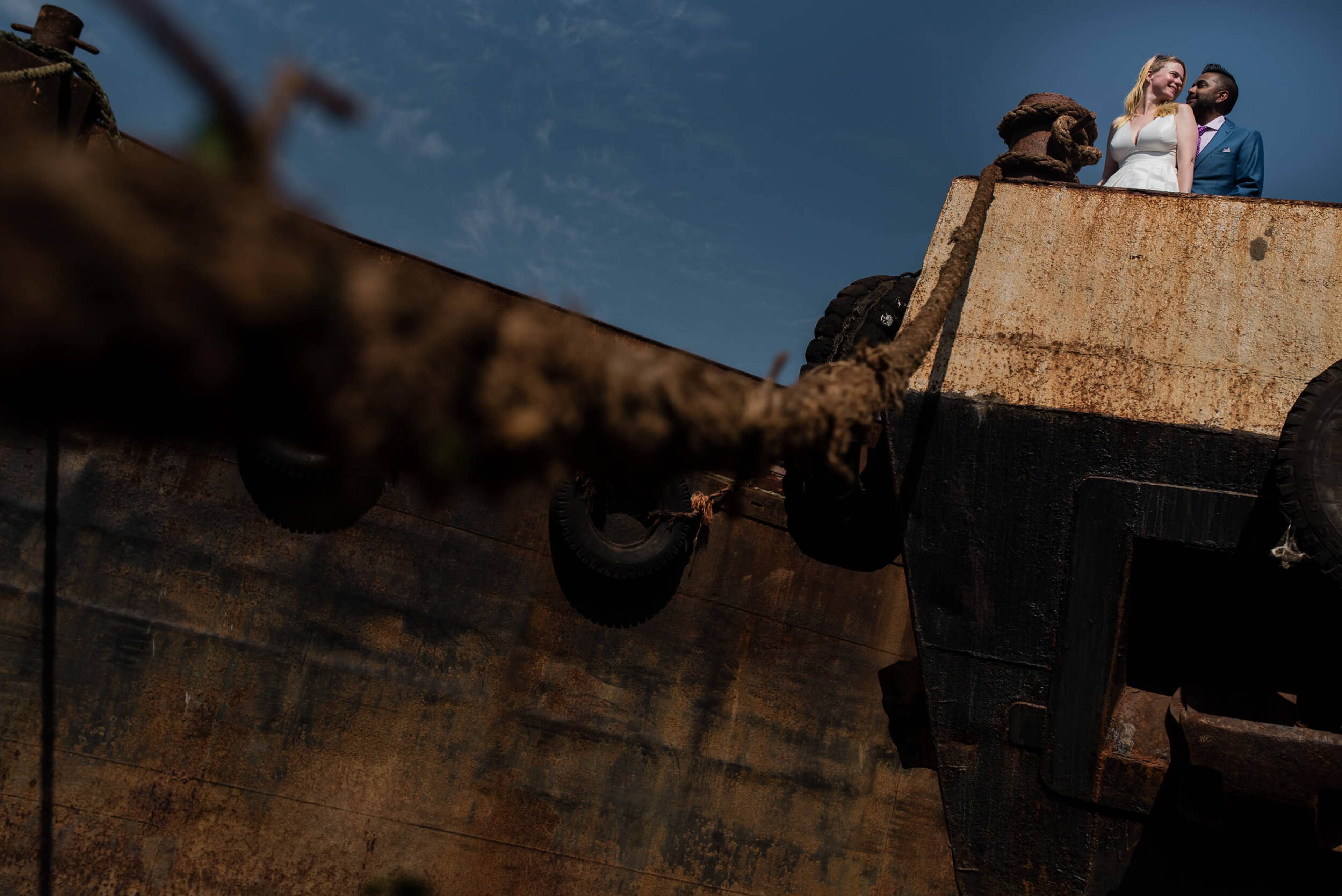 Couple stands on rusty industrial structure against blue sky in Goa