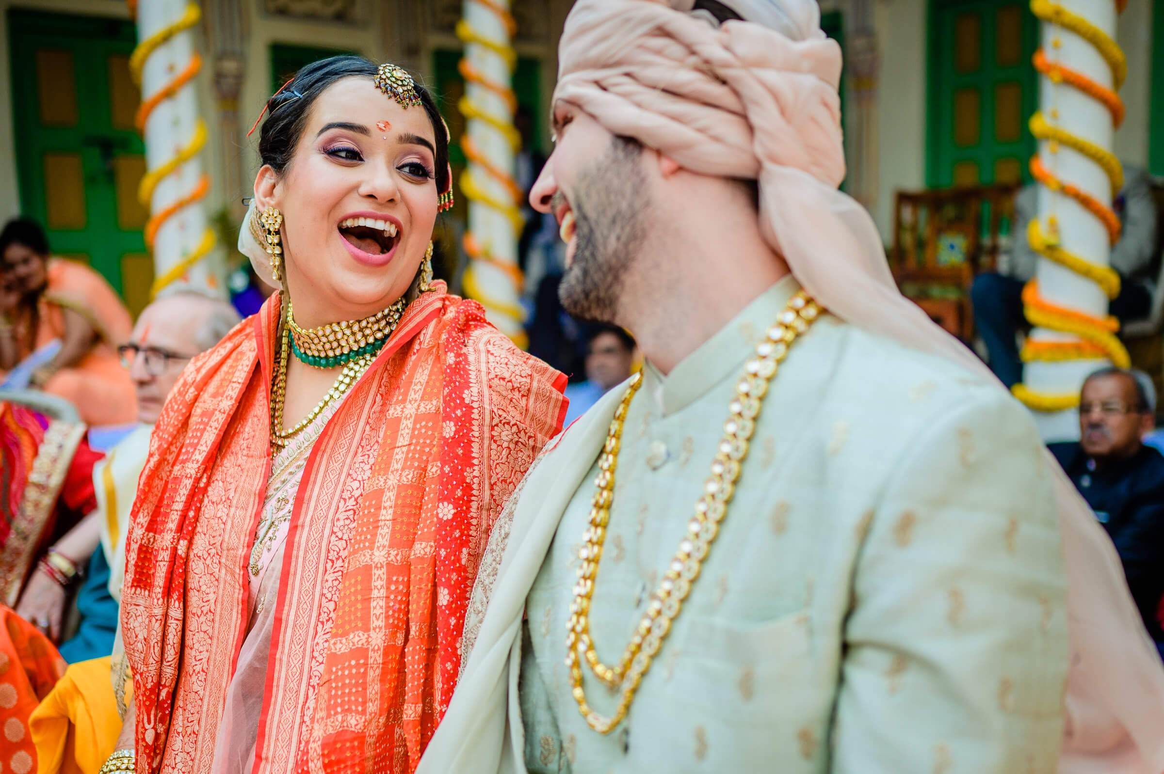 Maitrayee laughs joyfully while Eric covers his face during traditional Indian wedding ceremony in Rajasthan