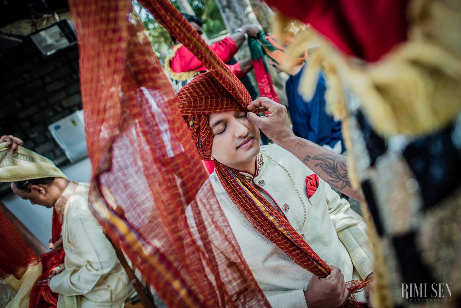 Groom Aniket in cream sherwani adjusting red turban during wedding ceremony in Bangalore