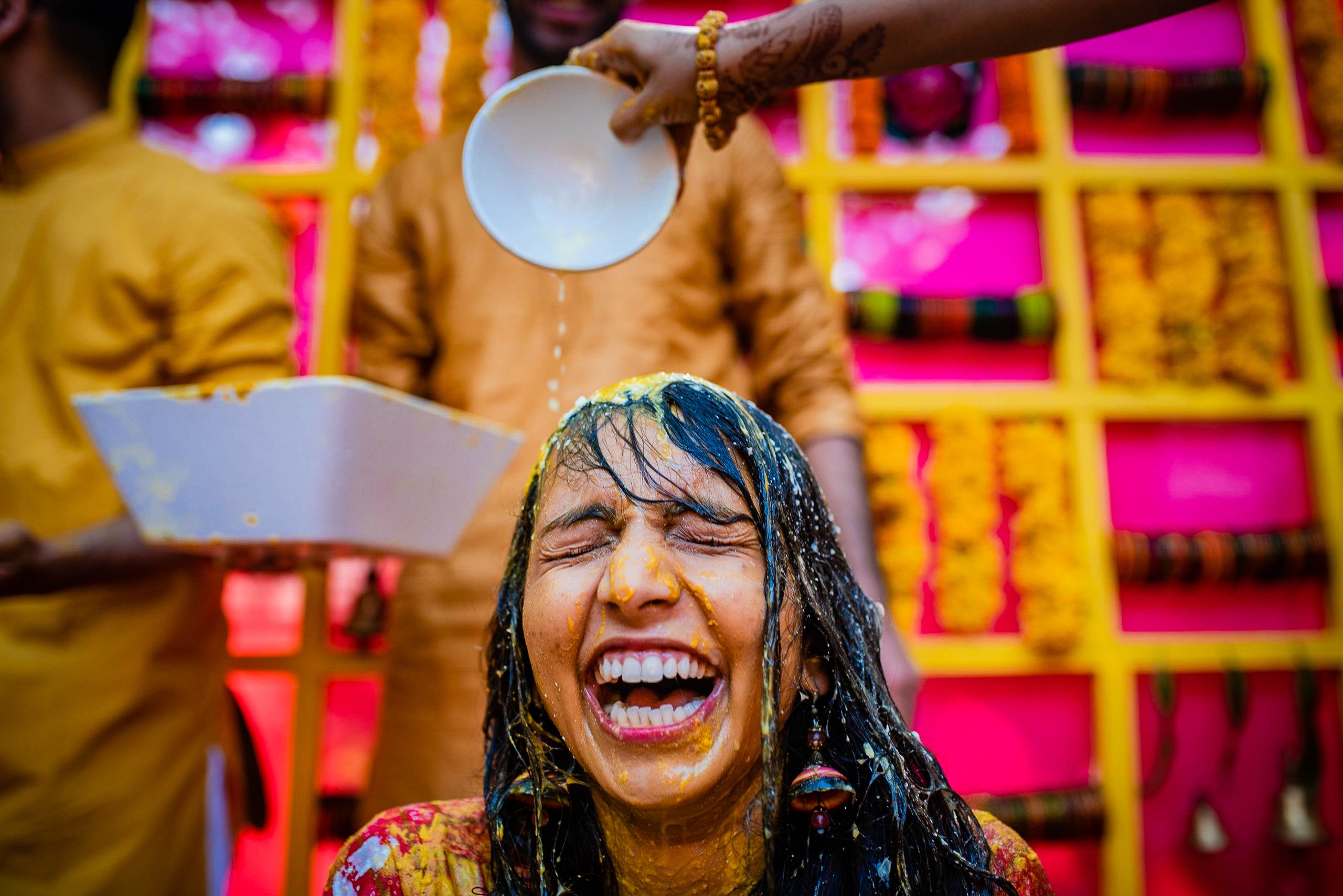 Avani laughs as water is poured over her head during Holi celebration in Goa, vibrant pink and yellow backdrop