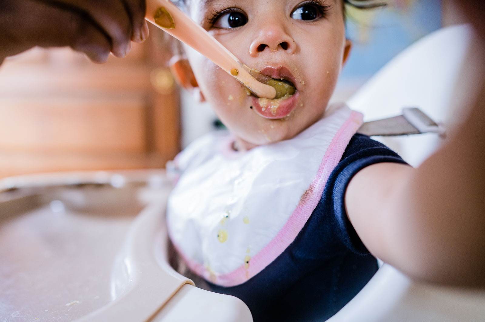 Toddler eating messy food with pink bib and wide-eyed expression