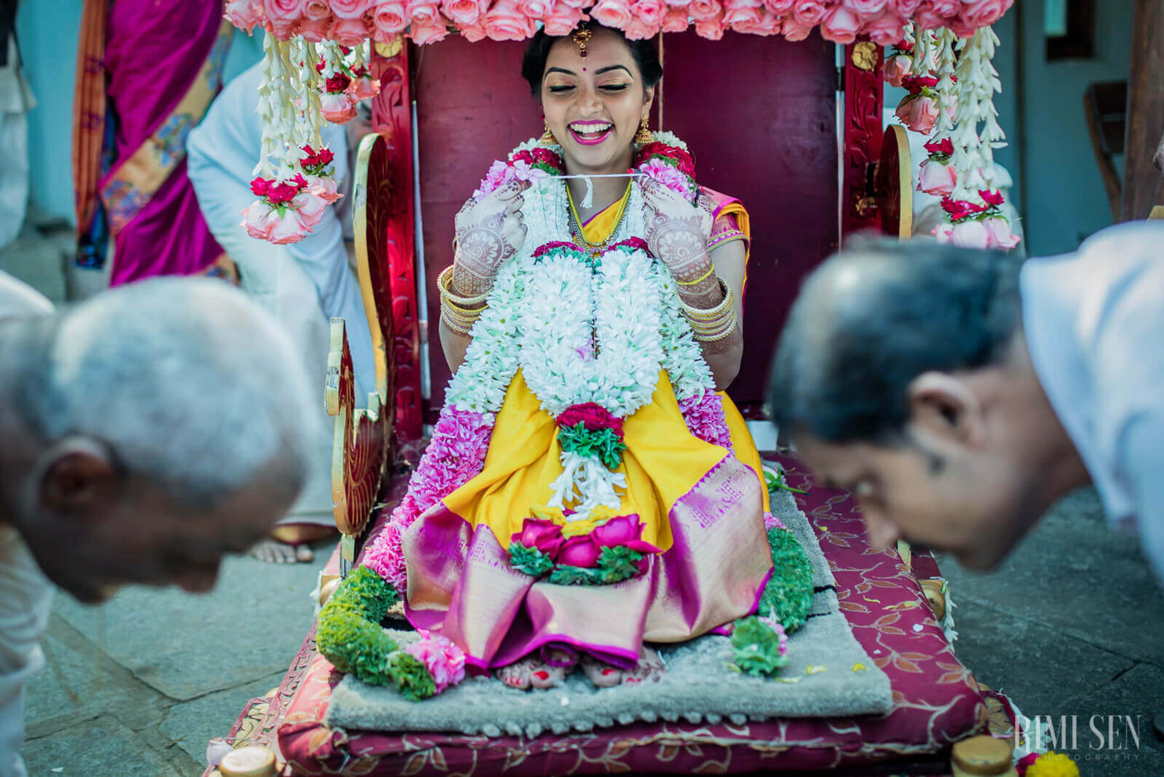 Pooja smiles brightly wearing yellow silk and white floral garland in traditional Indian wedding ceremony, Bangalore