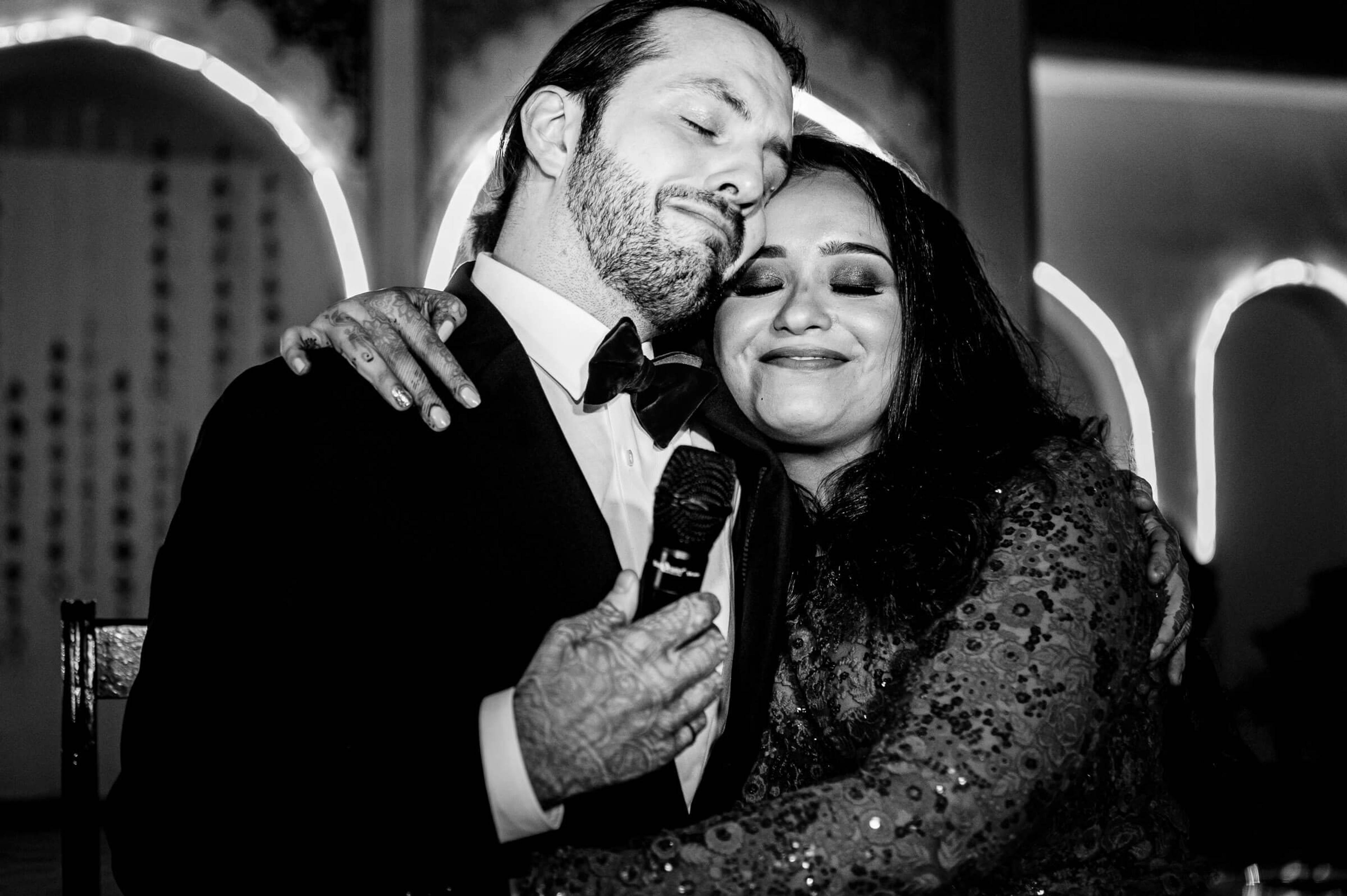 Maitrayee and Eric embrace under neon lights, black and white portrait with warm affection