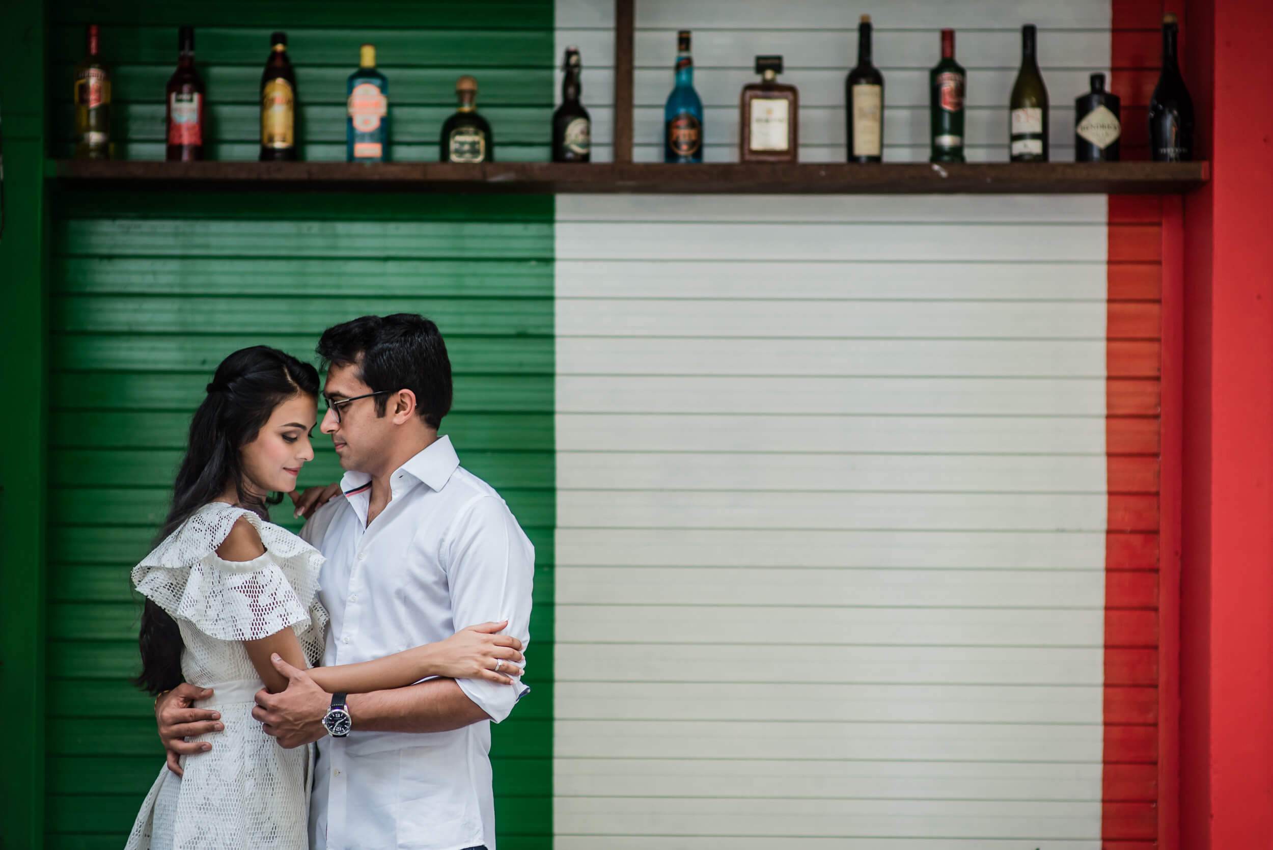 Yash and Disha embrace before a colorful bar wall in Singapore, intimate moment in soft light