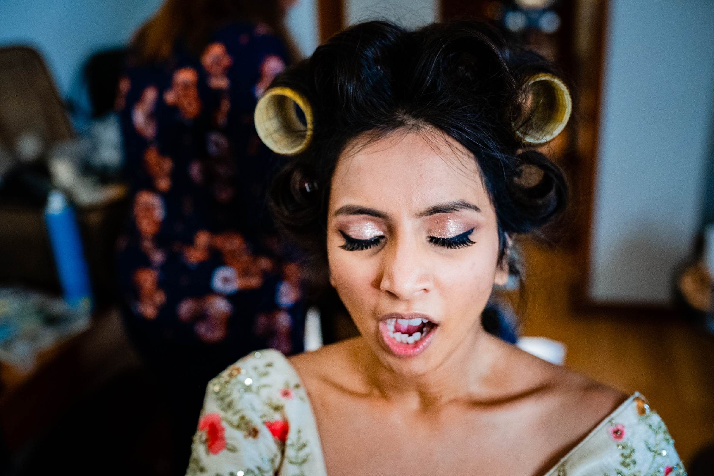 Avani in hair rollers and floral top, eyes closed, smiling during getting-ready moment in Goa