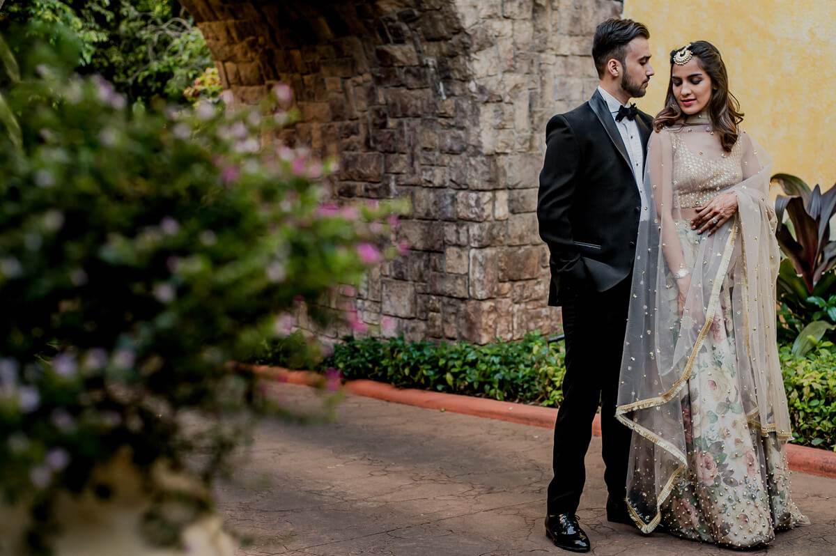 Shreya and Yash pose against stone walls and flowering vines in Mahabaleshwar's garden courtyard
