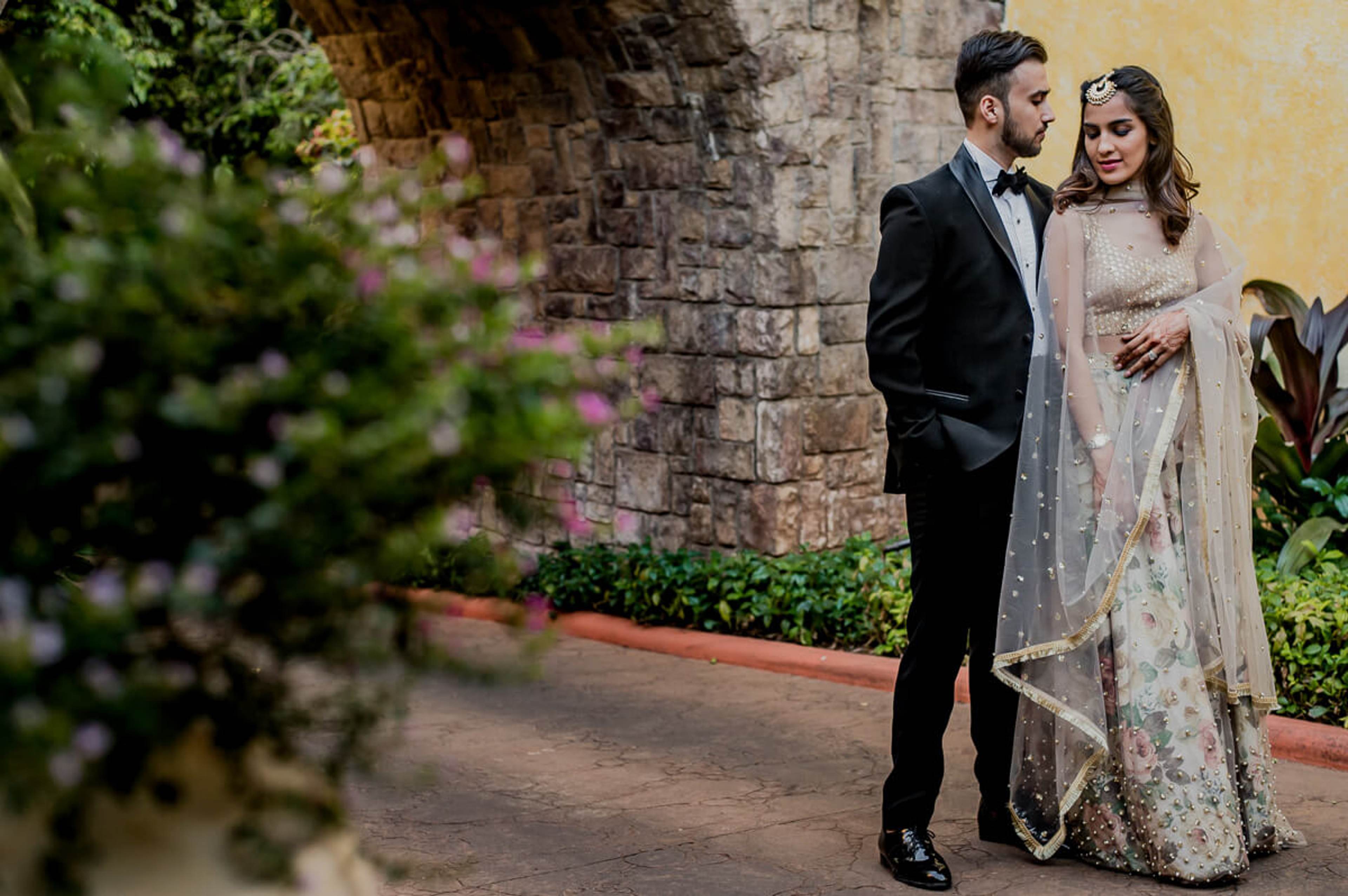 Shreya and Yash pose against stone walls and flowering vines in Mahabaleshwar's garden courtyard