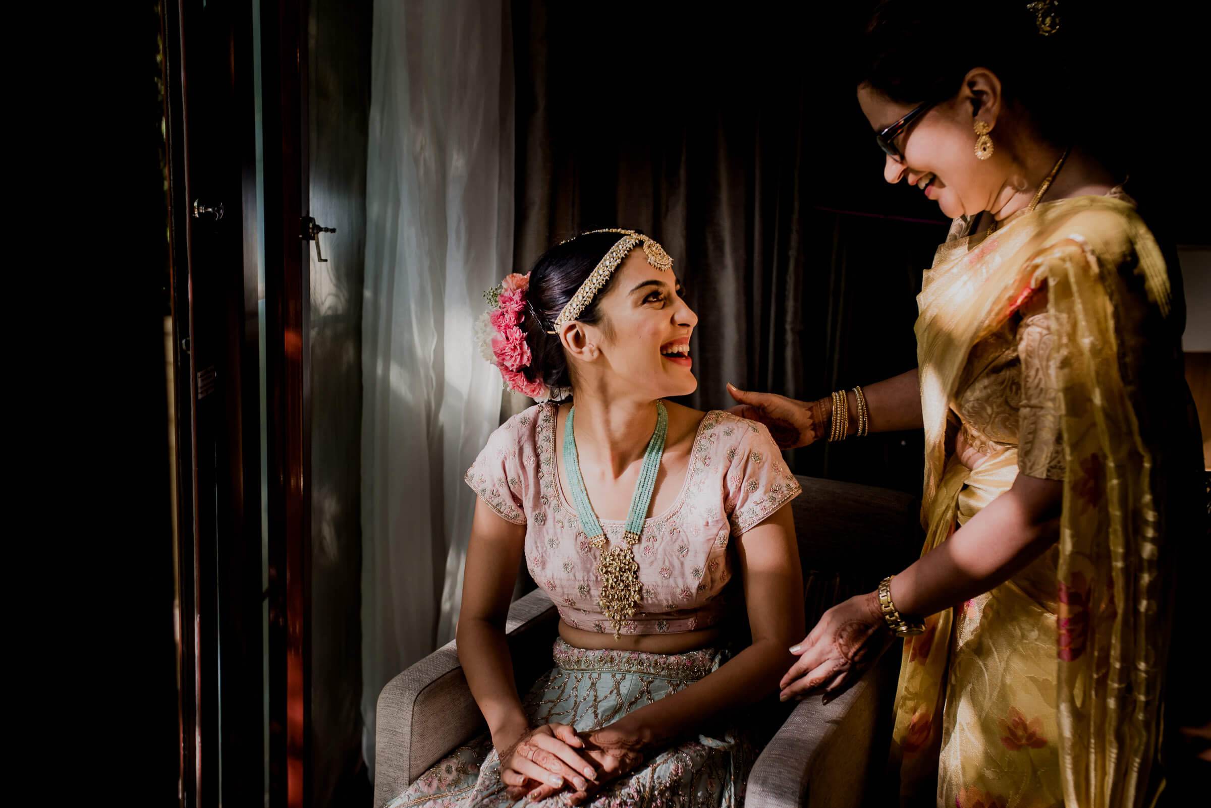 Shreya sits in pale pink traditional attire with pink flowers in her hair while Yash adjusts her gold dupatta in warm candlelight