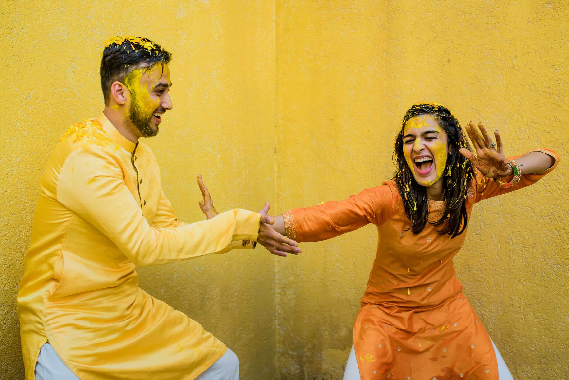 Shreya and Yash laugh and gesture playfully against a bright yellow wall in Mahabaleshwar
