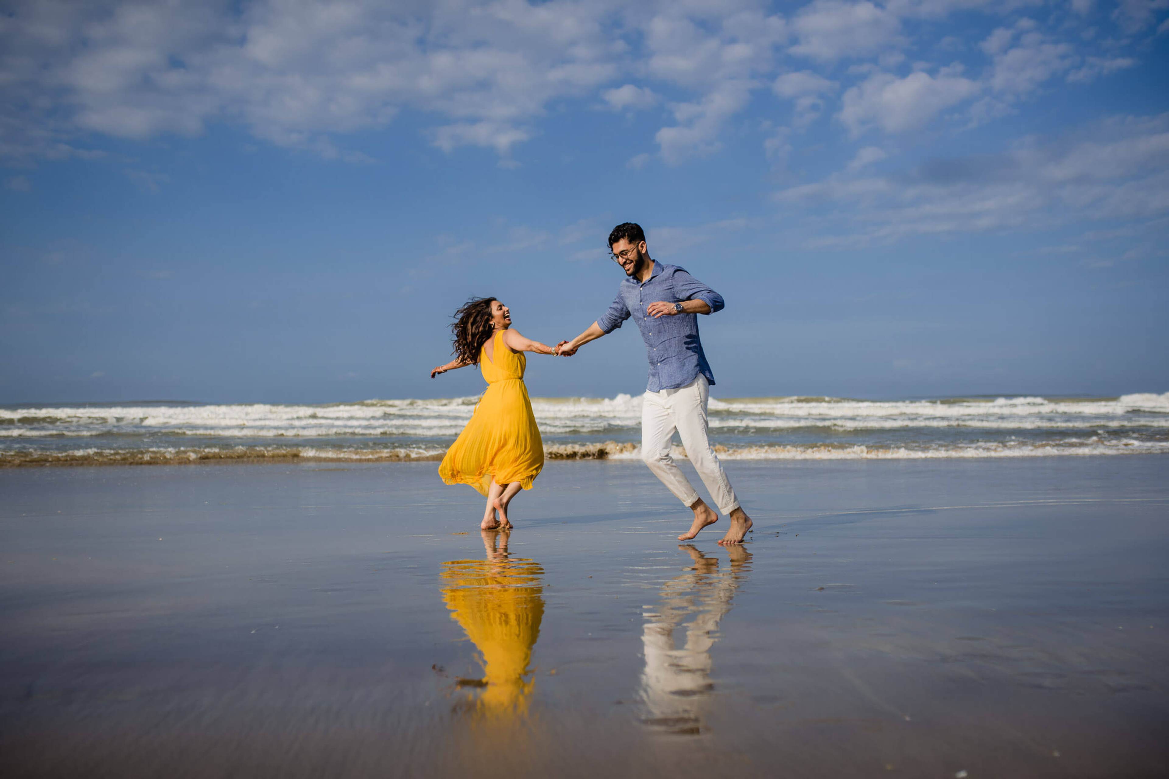 Couple dancing on wet beach sand with blue sky and ocean waves behind them