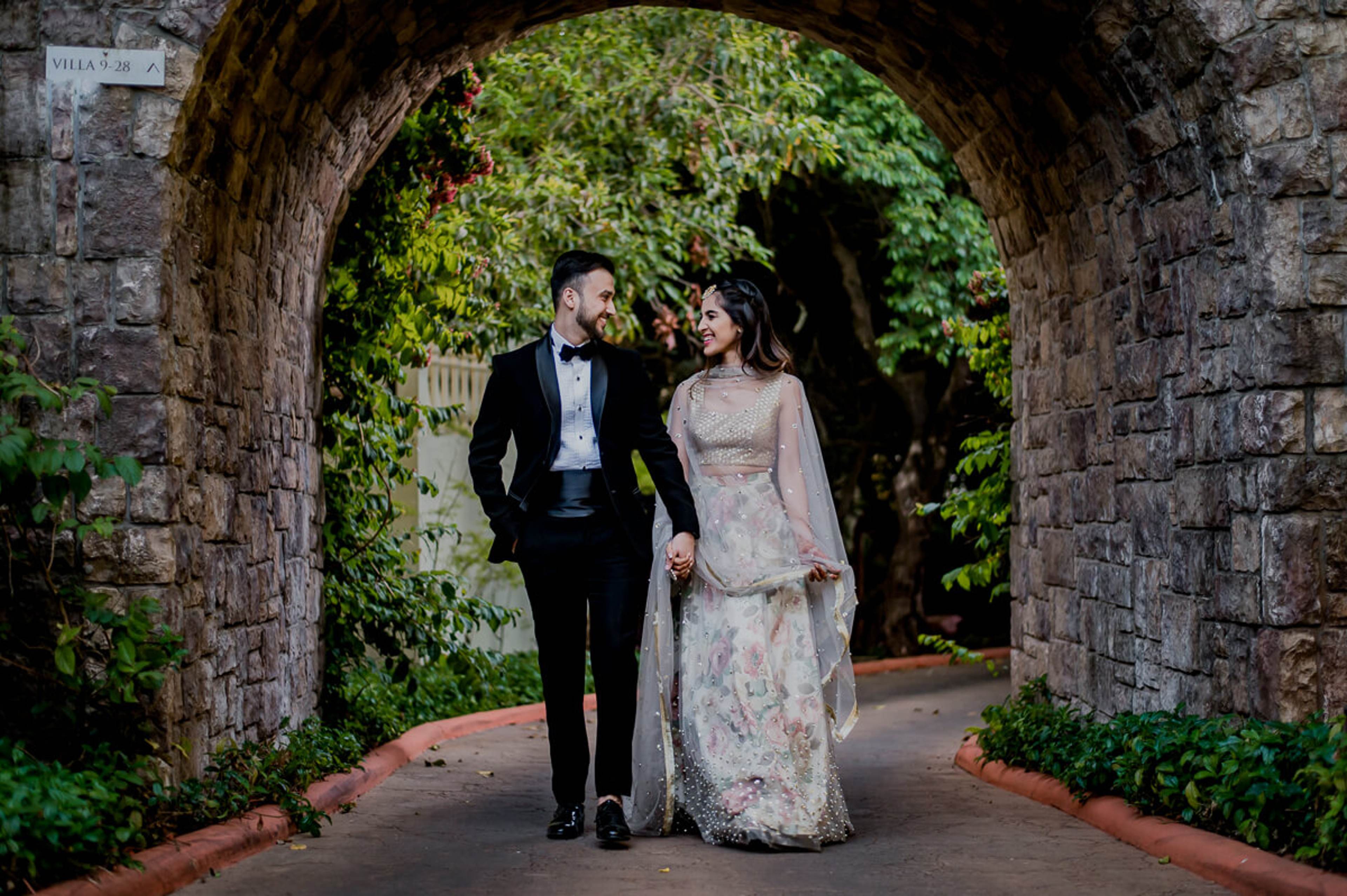 Shreya and Yash walk hand in hand through a lush ivy-covered stone archway at Mahabaleshwar