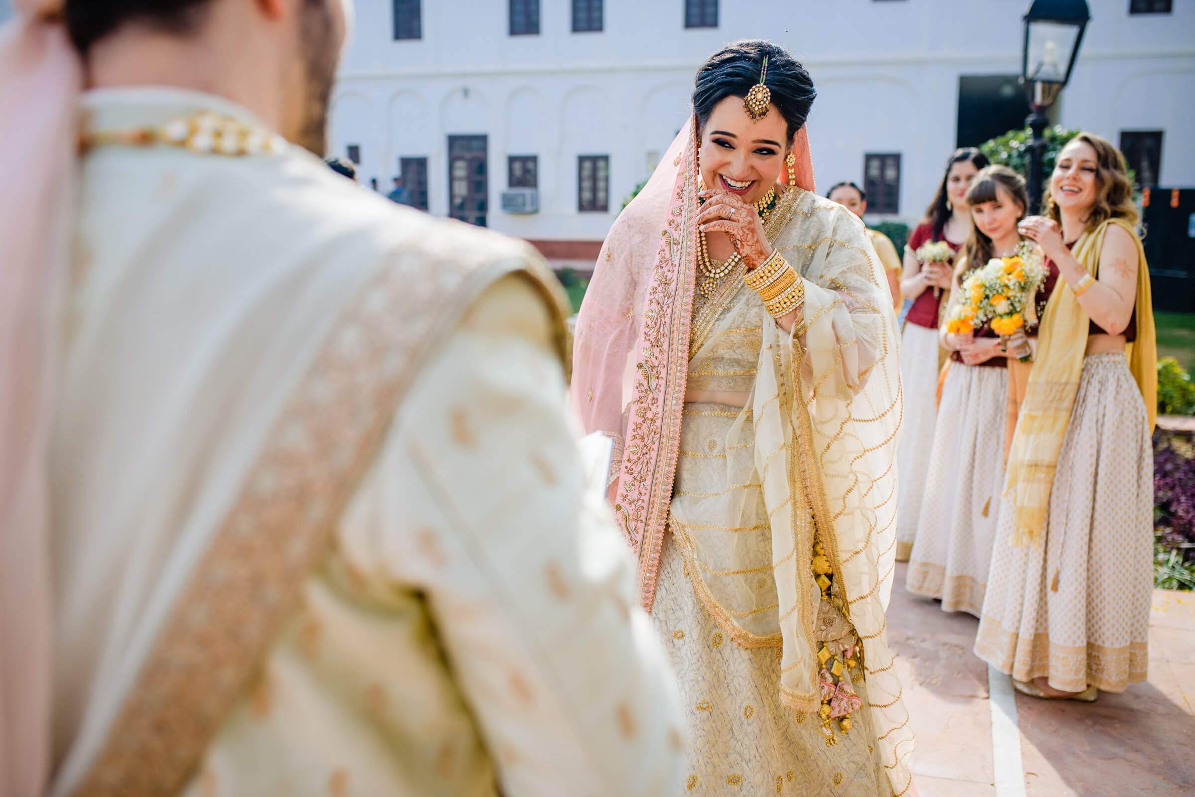 Maitrayee smiling in gold and pink wedding attire, facing Eric in traditional dress at Rajasthan ceremony