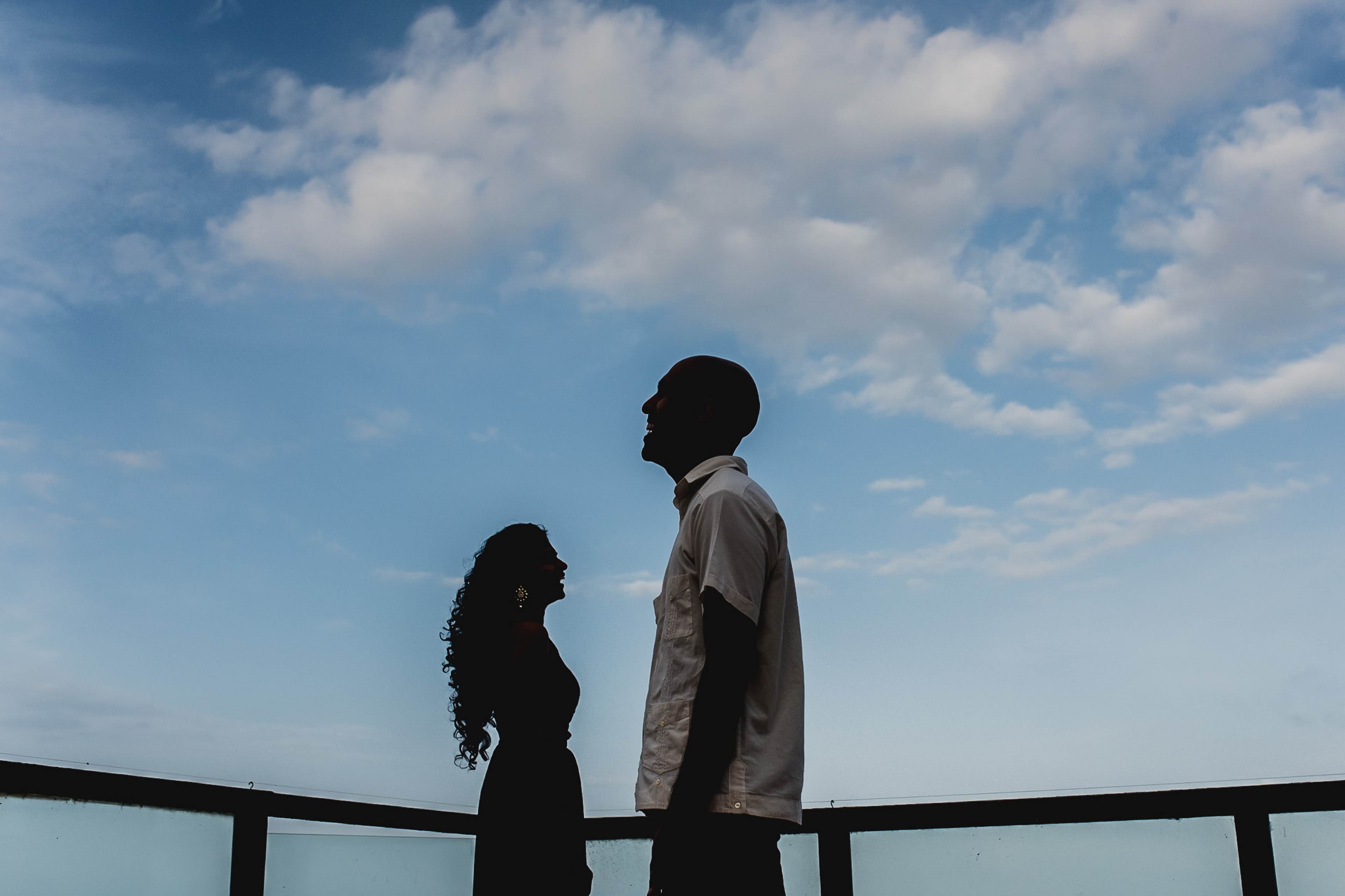 Shruthi and Rishi silhouetted against blue sky and clouds on a railing in Kerala by Rimi Sen