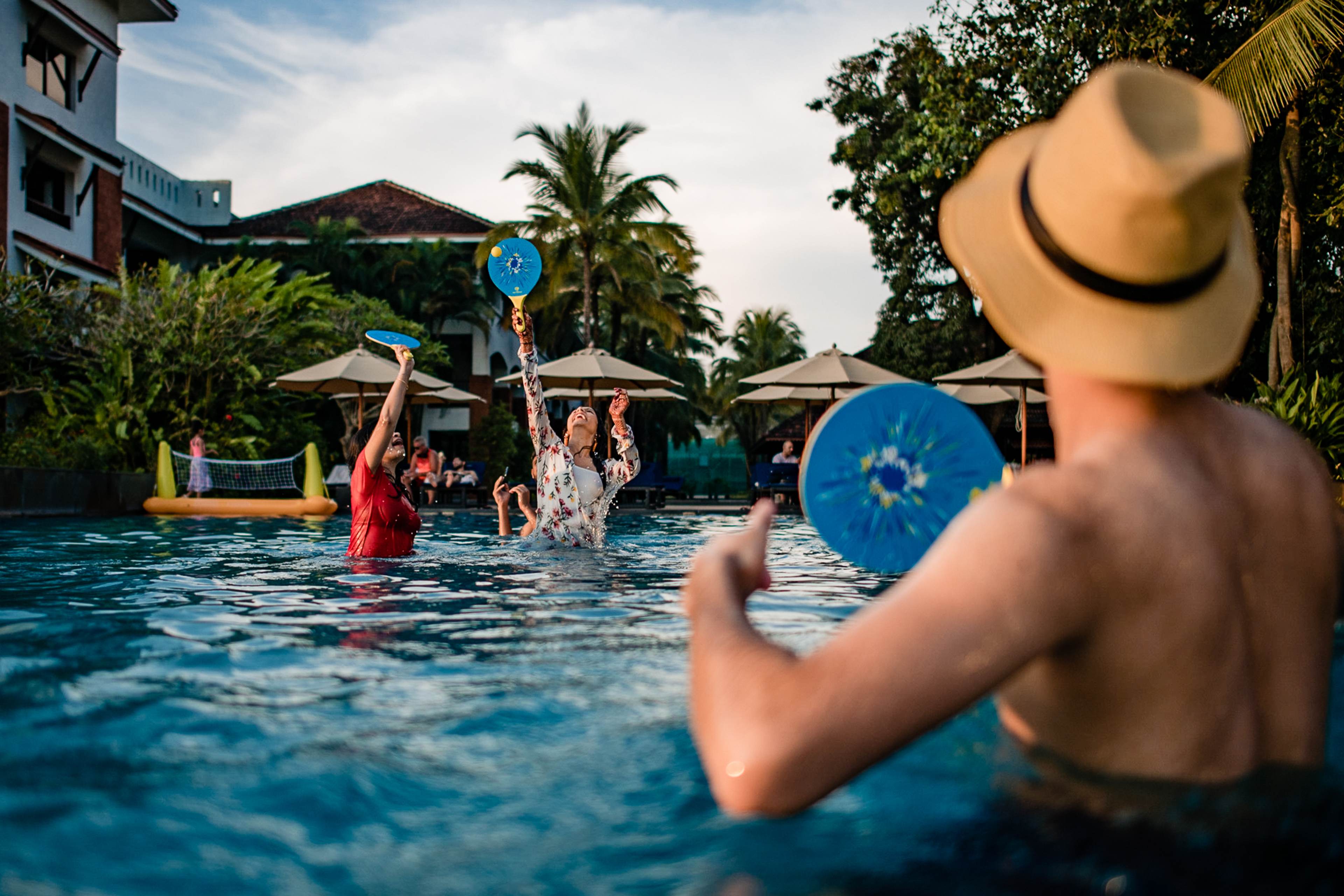 Avani & Srikant play with blue inflatables in a sunny Goa pool, tropical resort setting