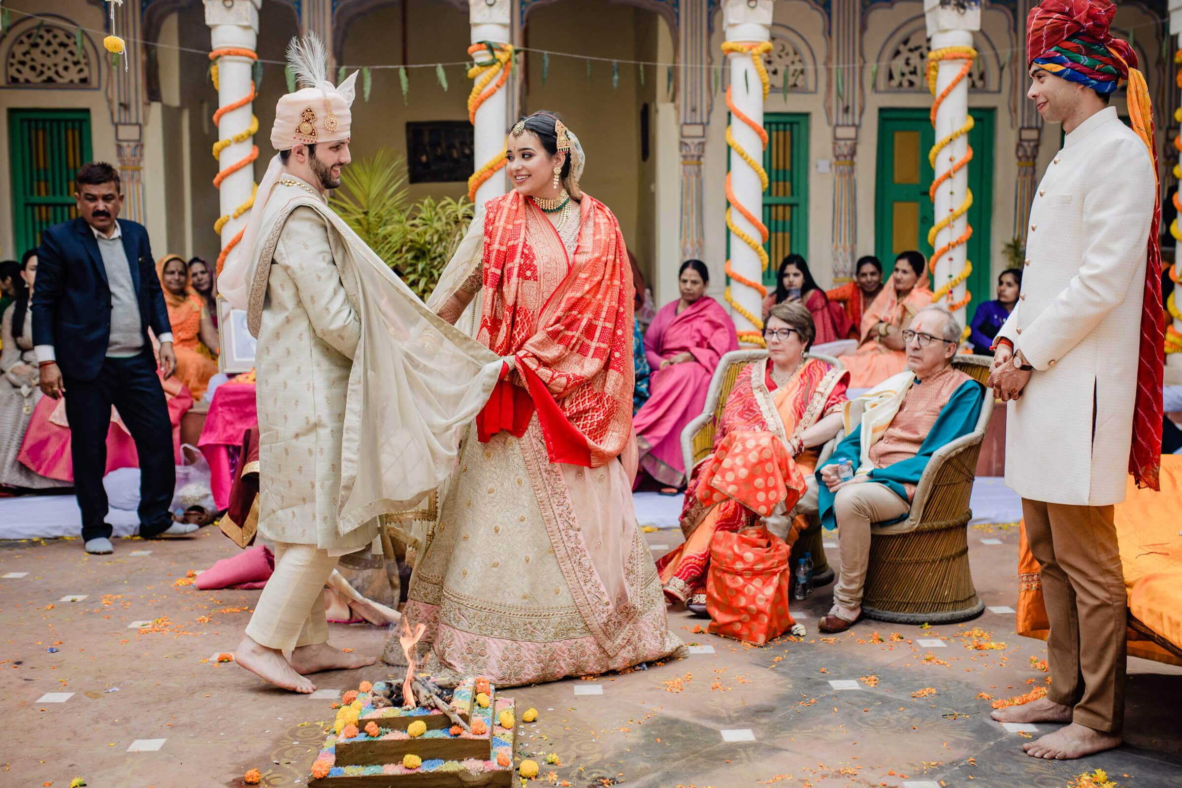 Maitrayee and Eric exchange garlands in traditional Rajasthani attire at a vibrant courtyard ceremony in Rajasthan