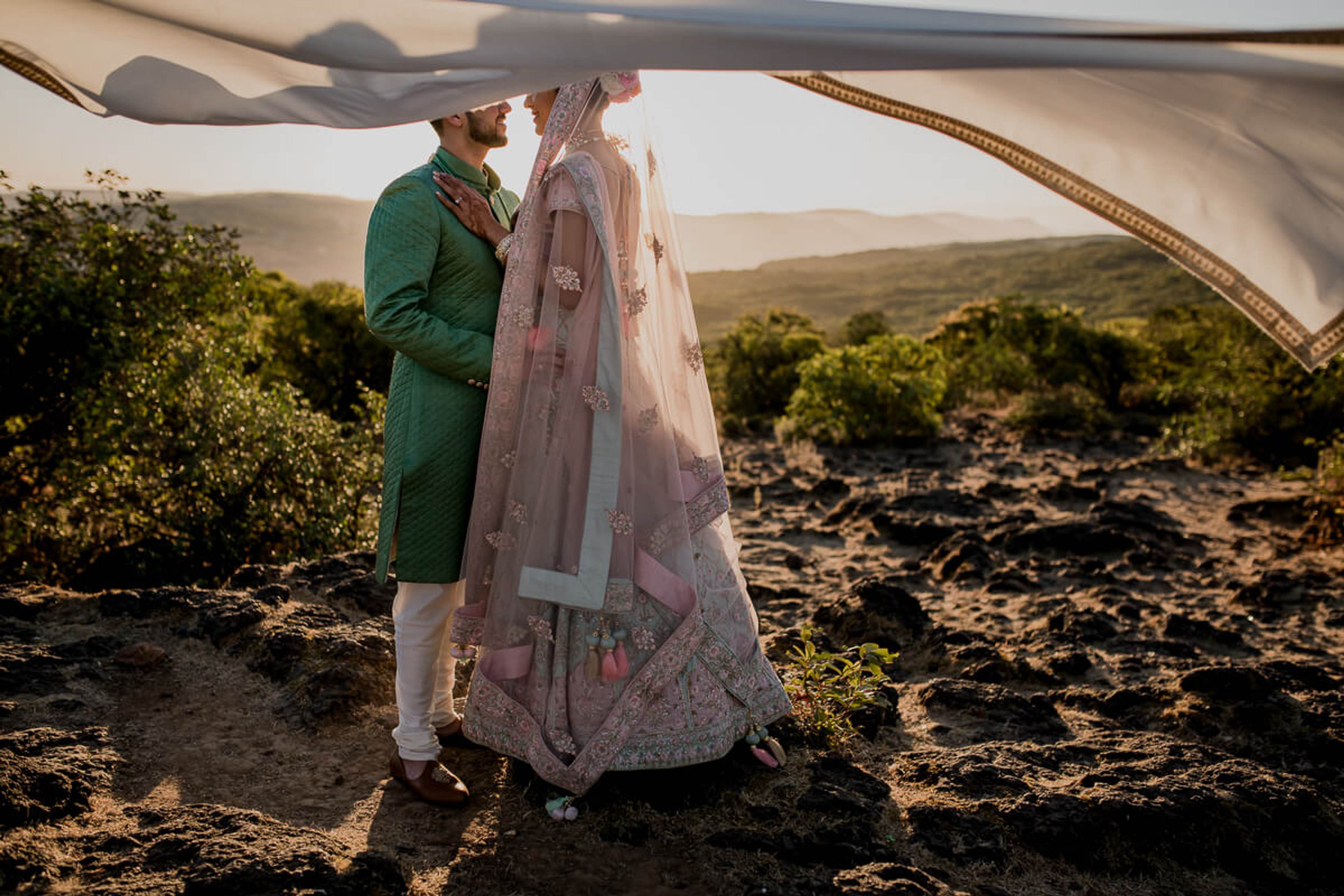 Shreya and Yash embrace under sheer fabric tent, hills visible beyond, golden light at Mahabaleshwar