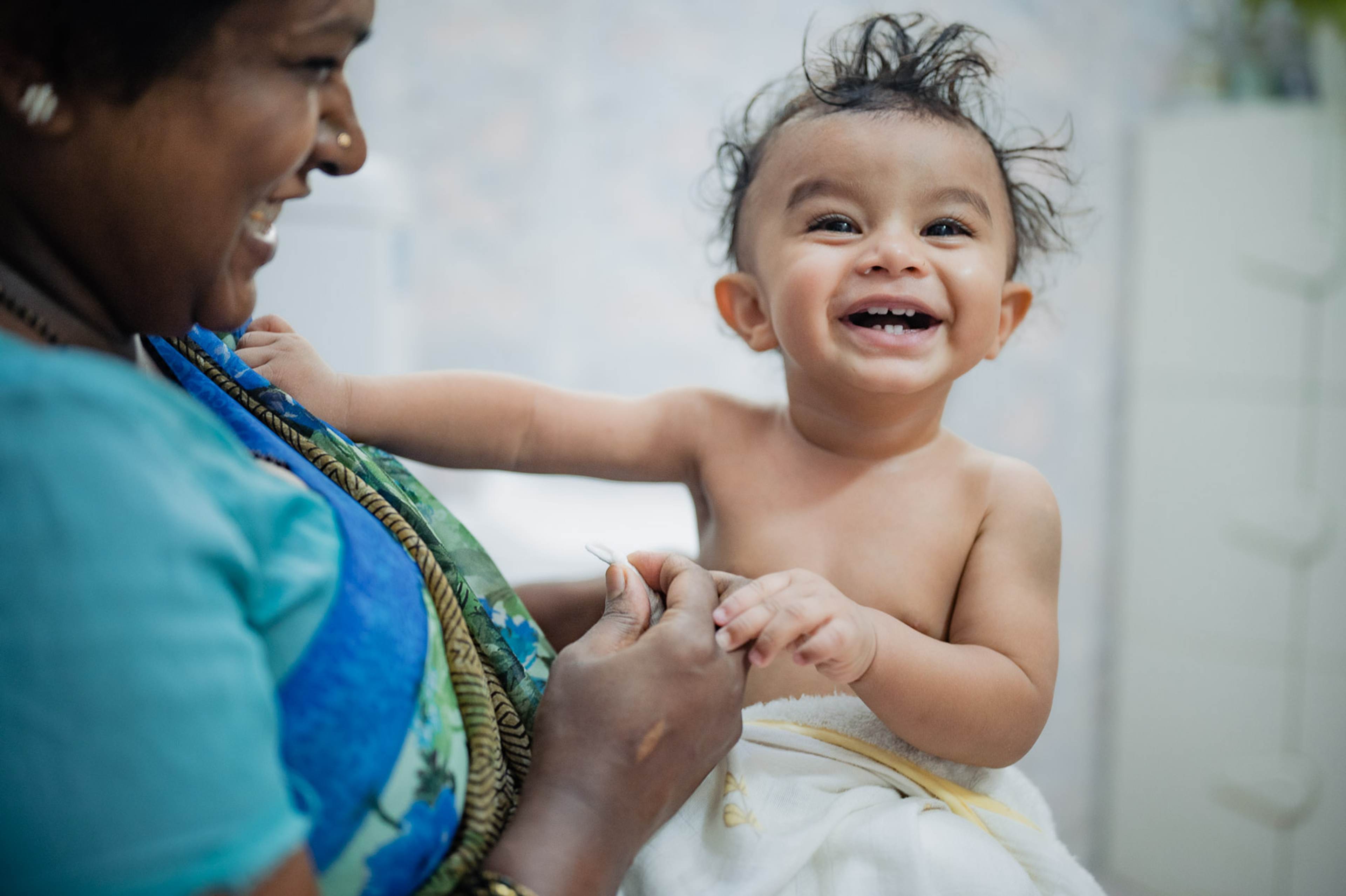 Woman in blue shirt holding smiling toddler with dark hair indoors