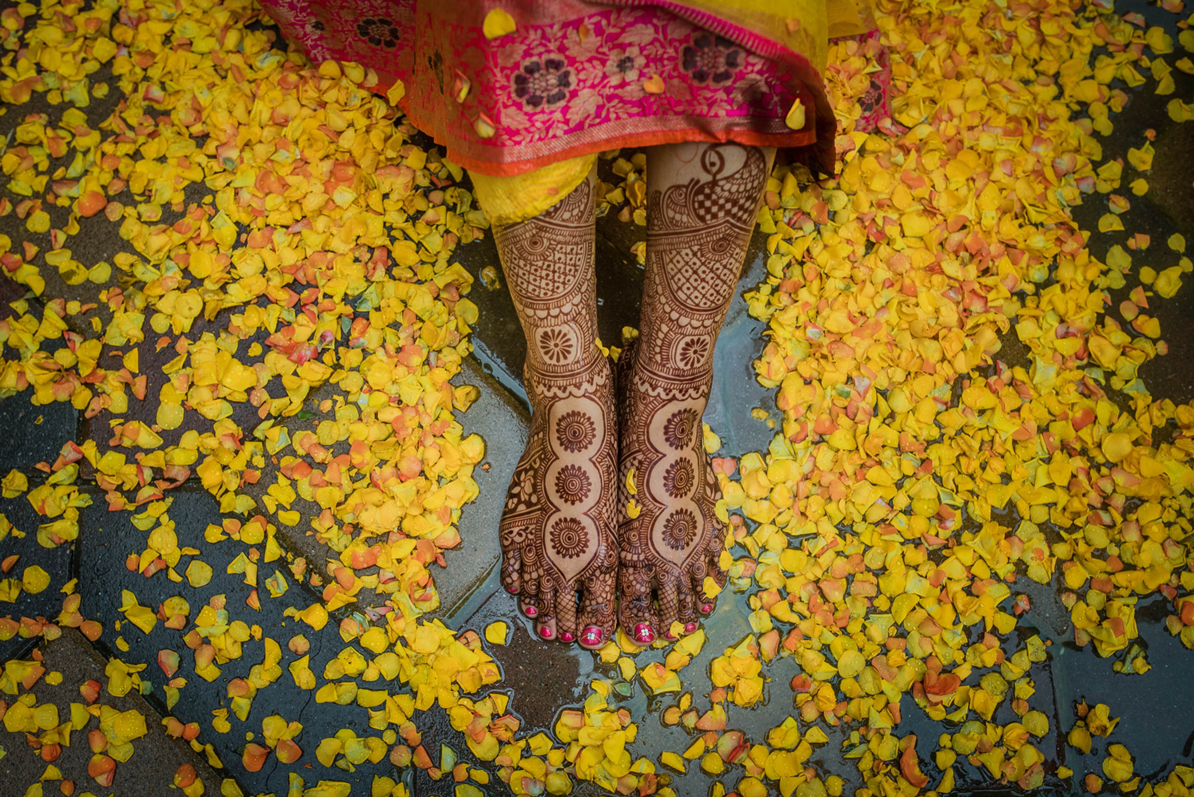 Bride's hennaed feet and legs surrounded by yellow flower petals, wearing pink silk fabric