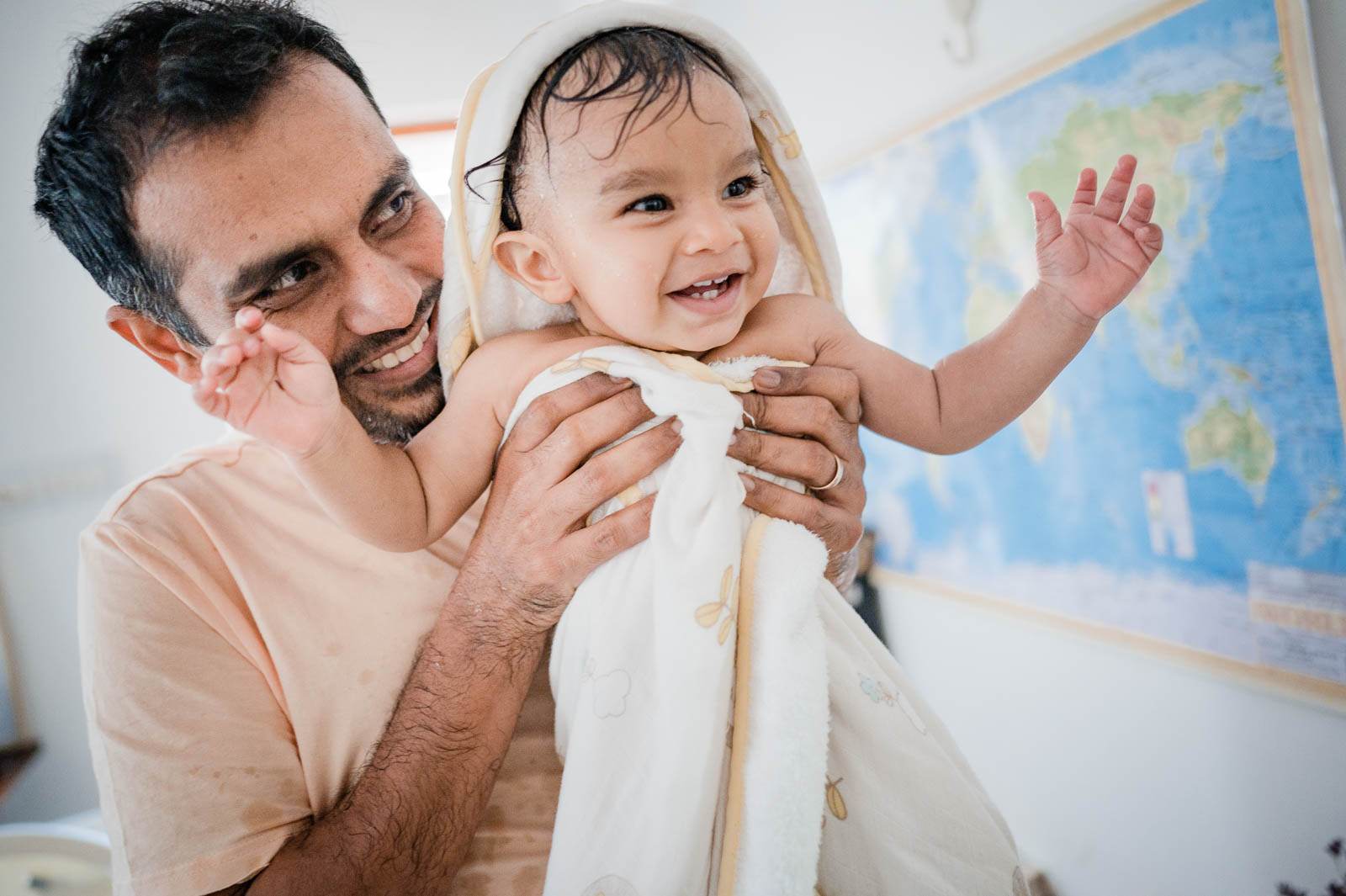 Father holding smiling toddler wrapped in white towel, world map visible behind them