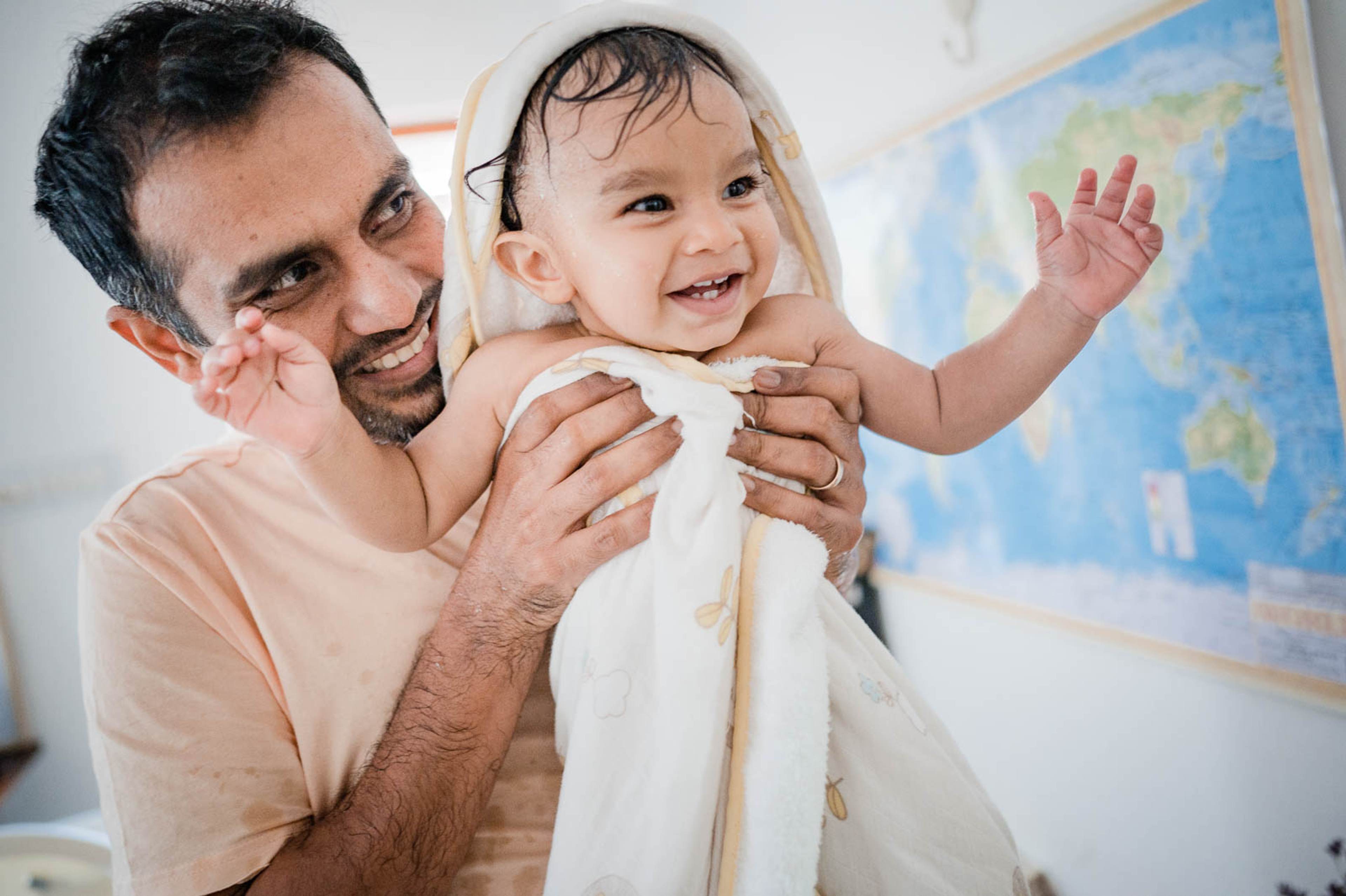 Father holding smiling toddler wrapped in white towel, world map visible behind them