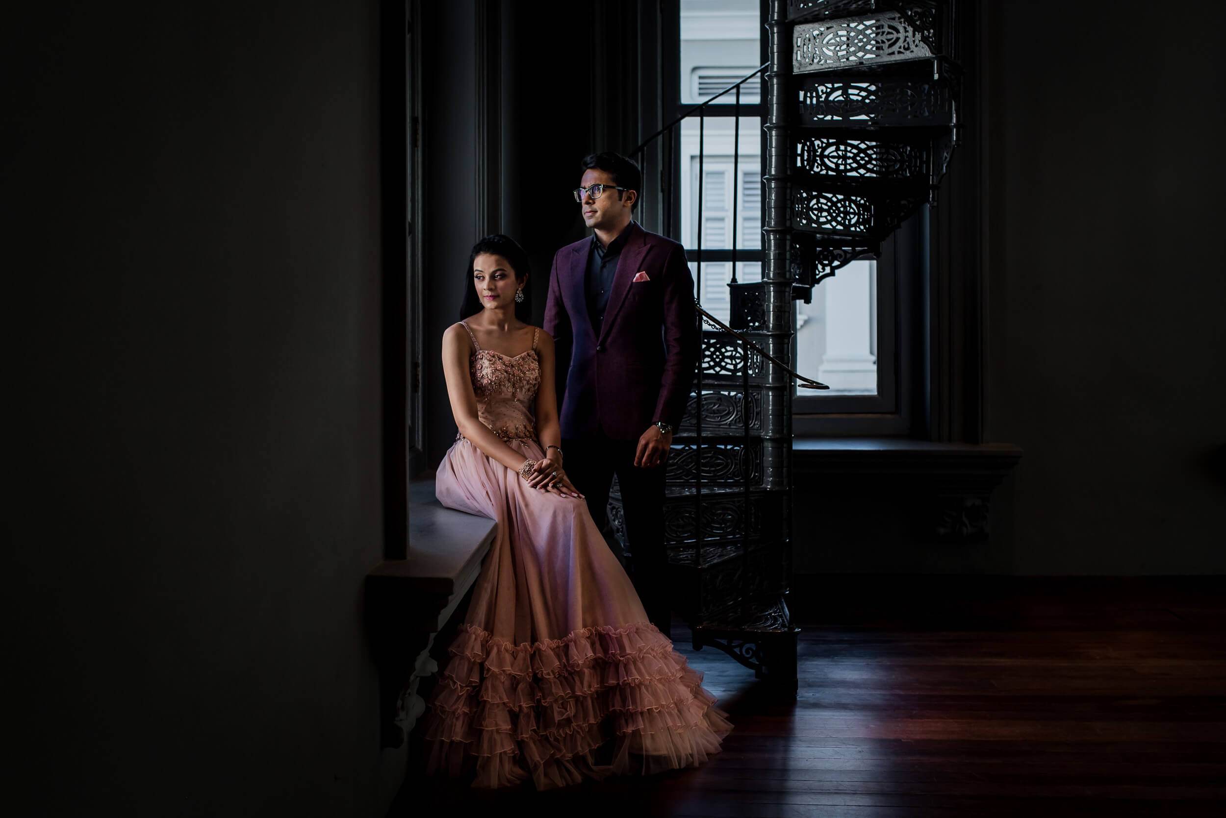 Yash & Disha pose elegantly in a dark interior space with ornate black screen and natural light from window