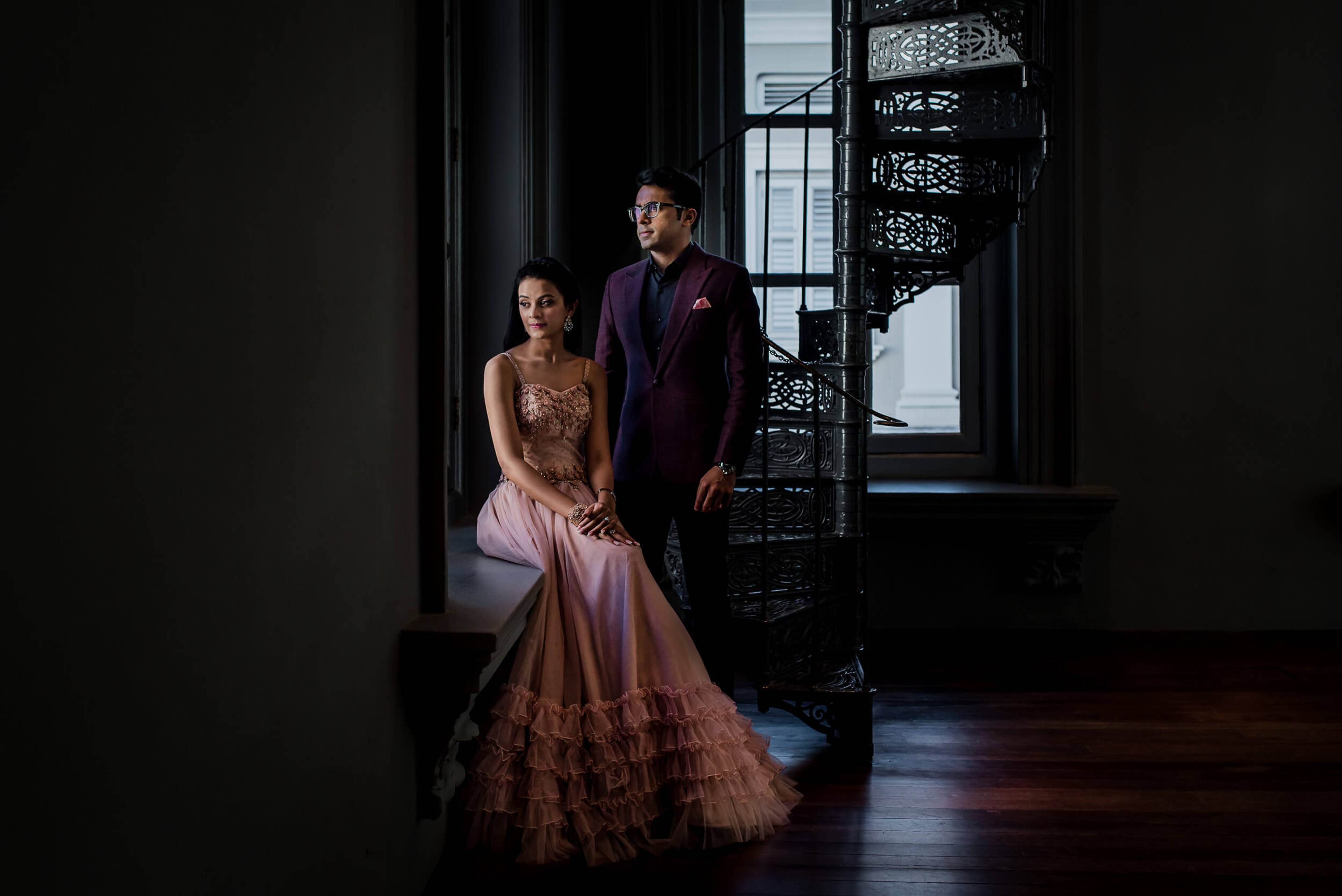 Yash & Disha pose elegantly in a dark interior space with ornate black screen and natural light from window