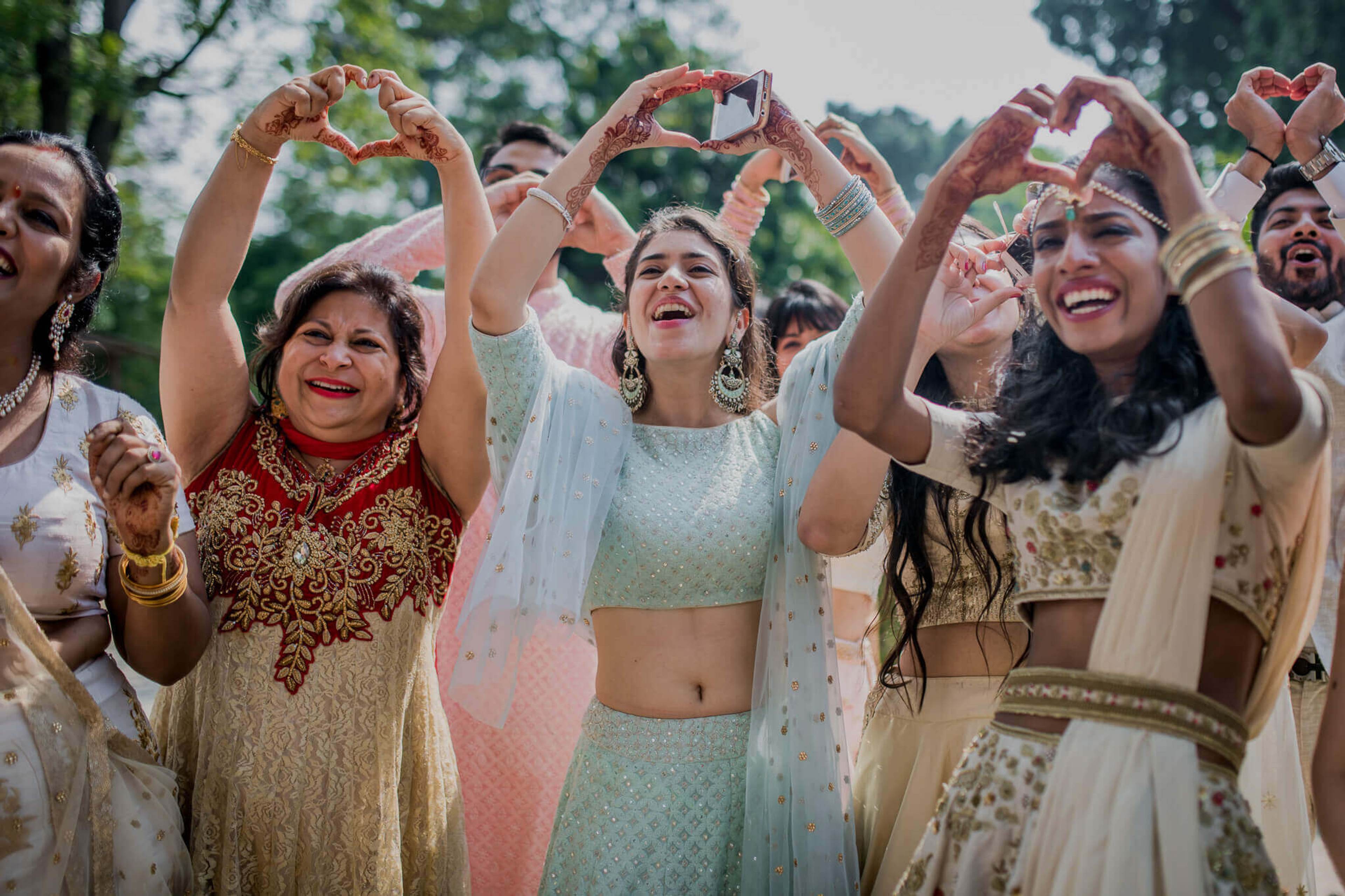 Group of smiling women in traditional Indian attire making heart shapes with hands outdoors in Nepal