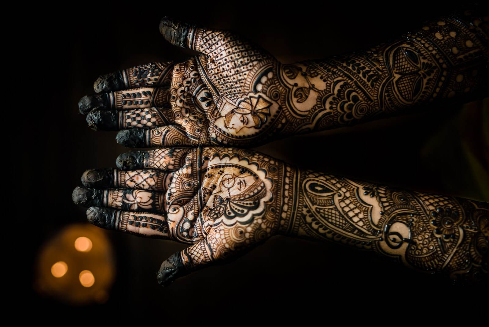 Barkha's ornate henna-decorated hands with traditional bangles against dark background