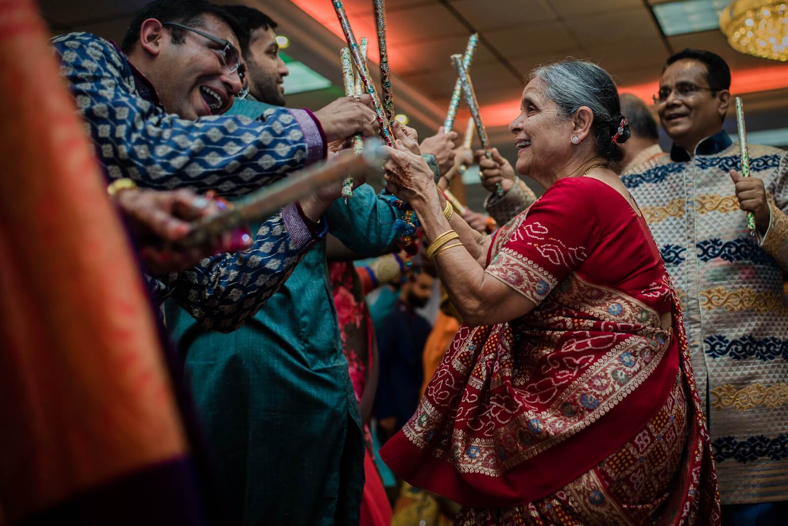 Barkha and Ankit celebrate with family, holding decorative sticks in traditional attire at New York wedding reception