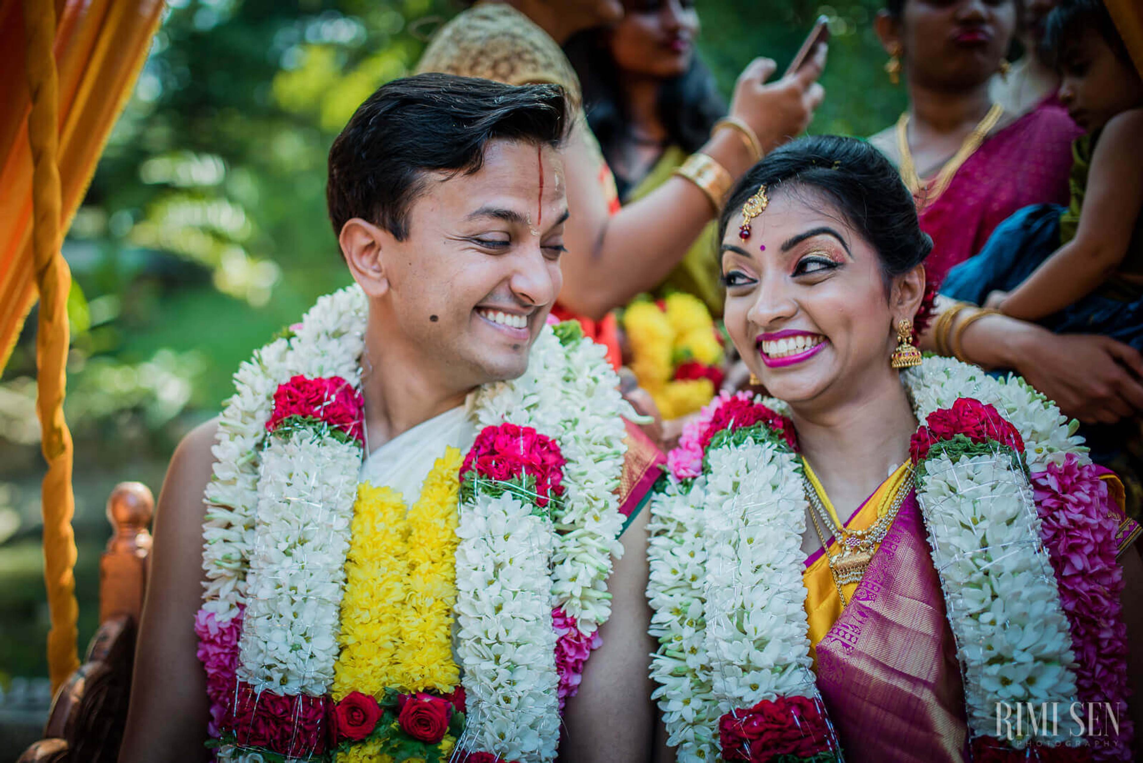 Pooja and Aniket smiling in white, pink, and yellow flower garlands at their Bangalore wedding ceremony