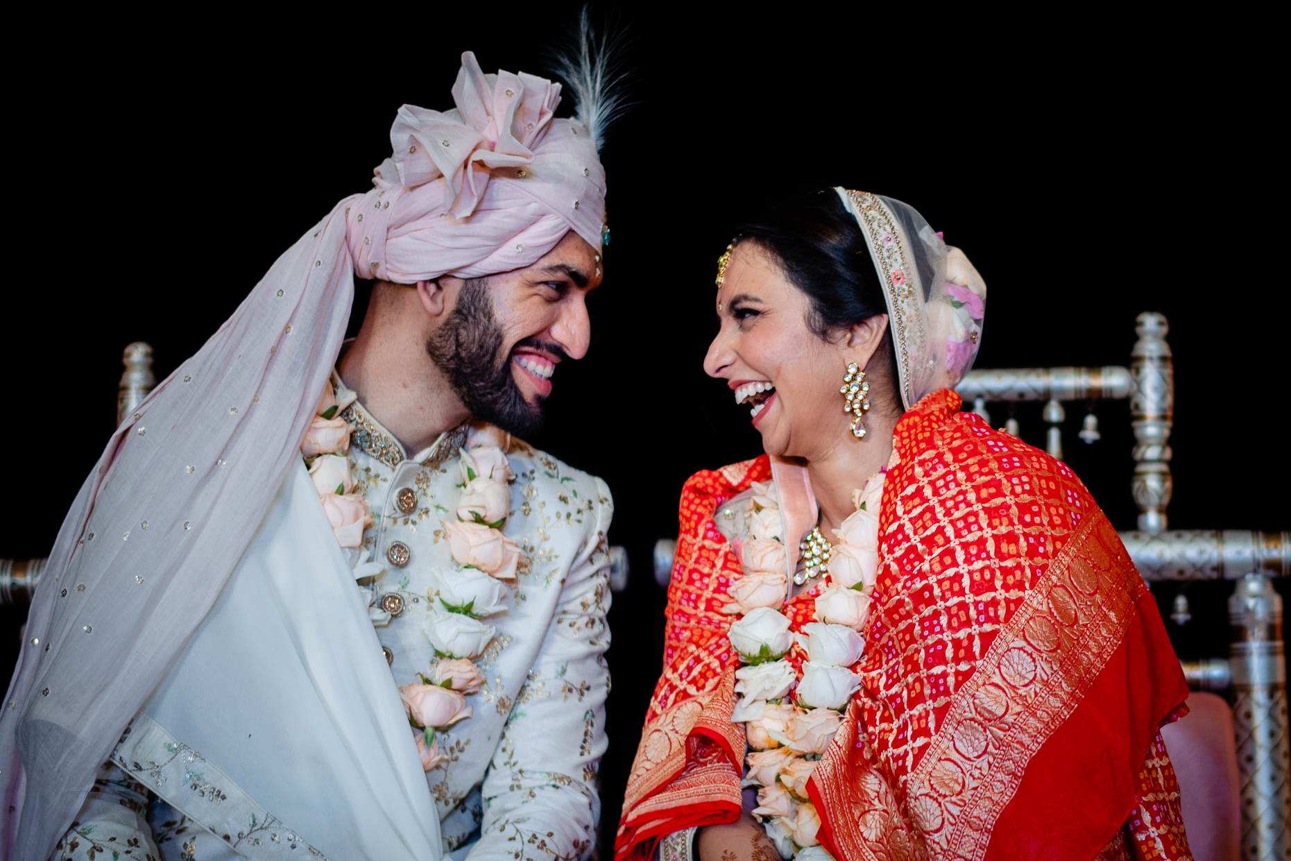 Avani and Srikant smile at each other in traditional wedding attire with flower garlands, Goa