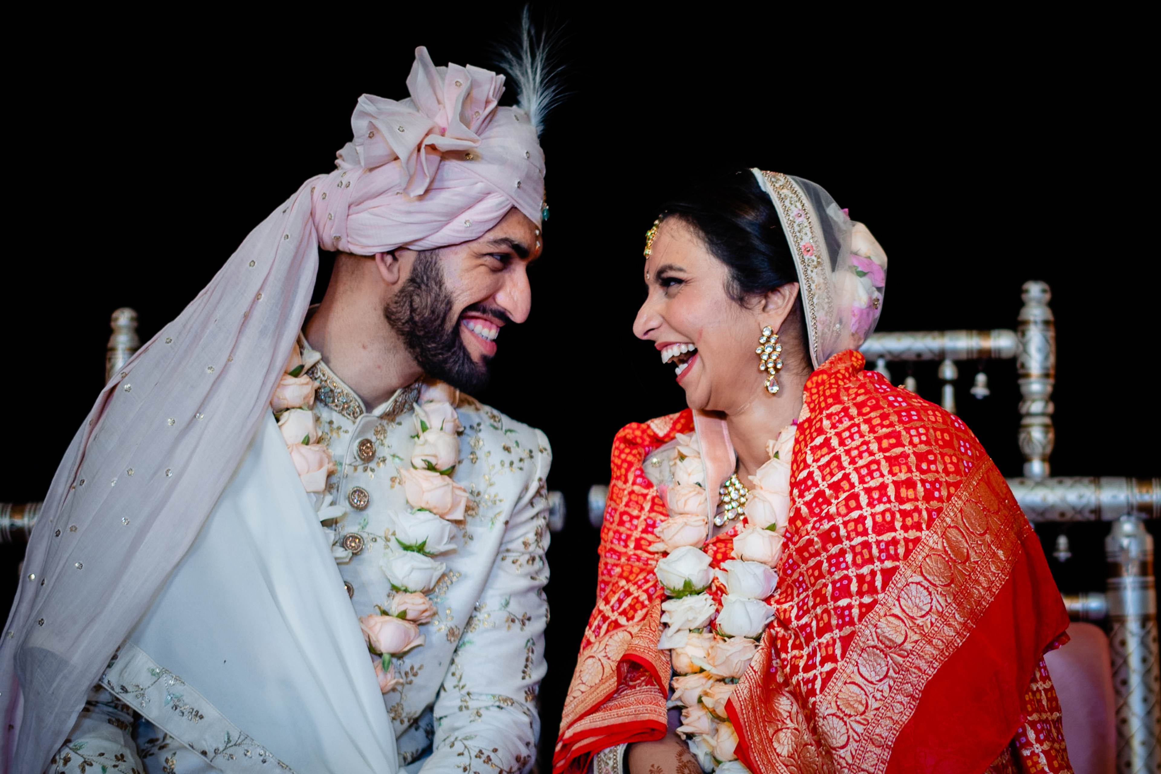 Avani and Srikant smile at each other in traditional wedding attire with flower garlands, Goa