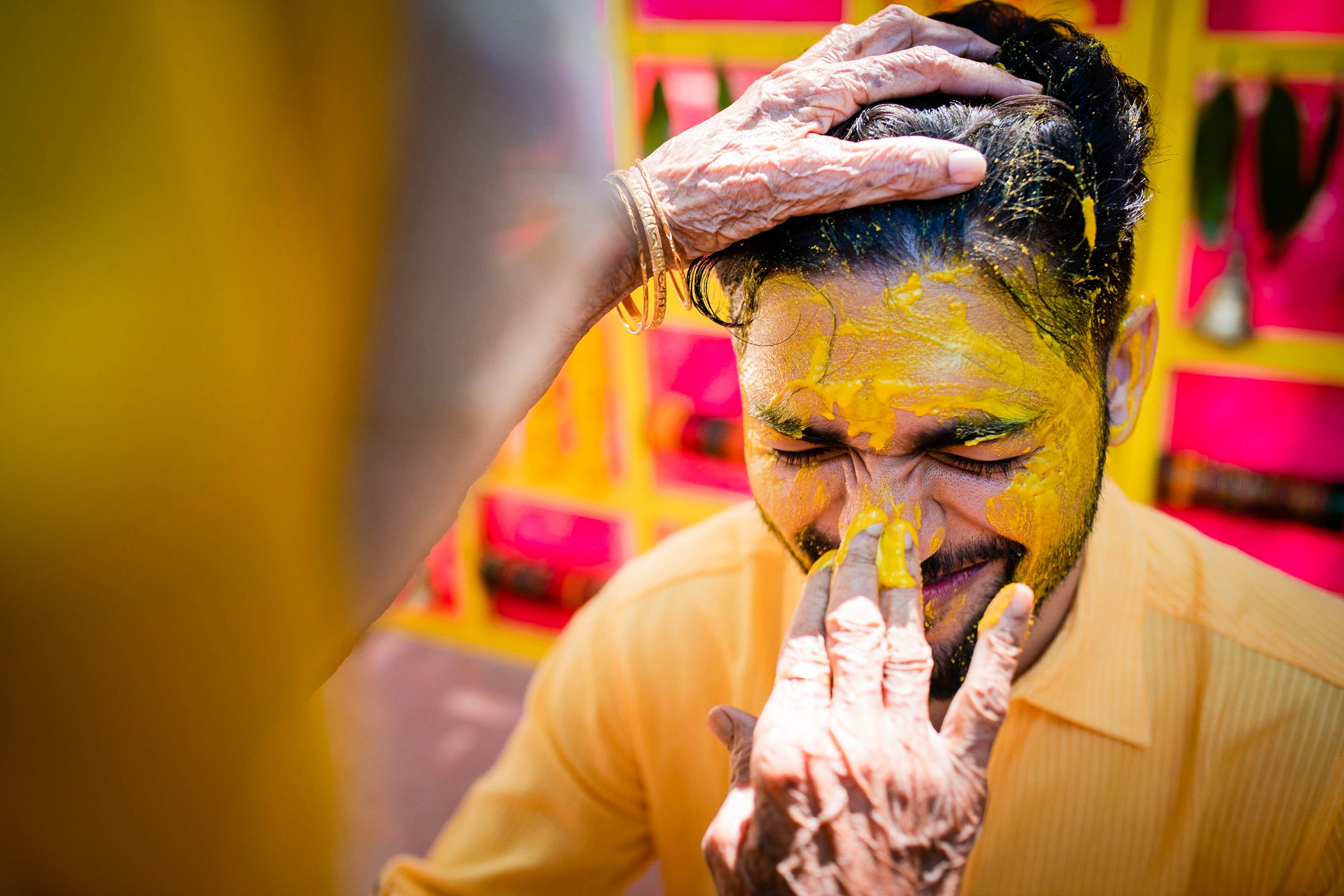 Man smiling while applying yellow and pink colored powder to his face during celebration