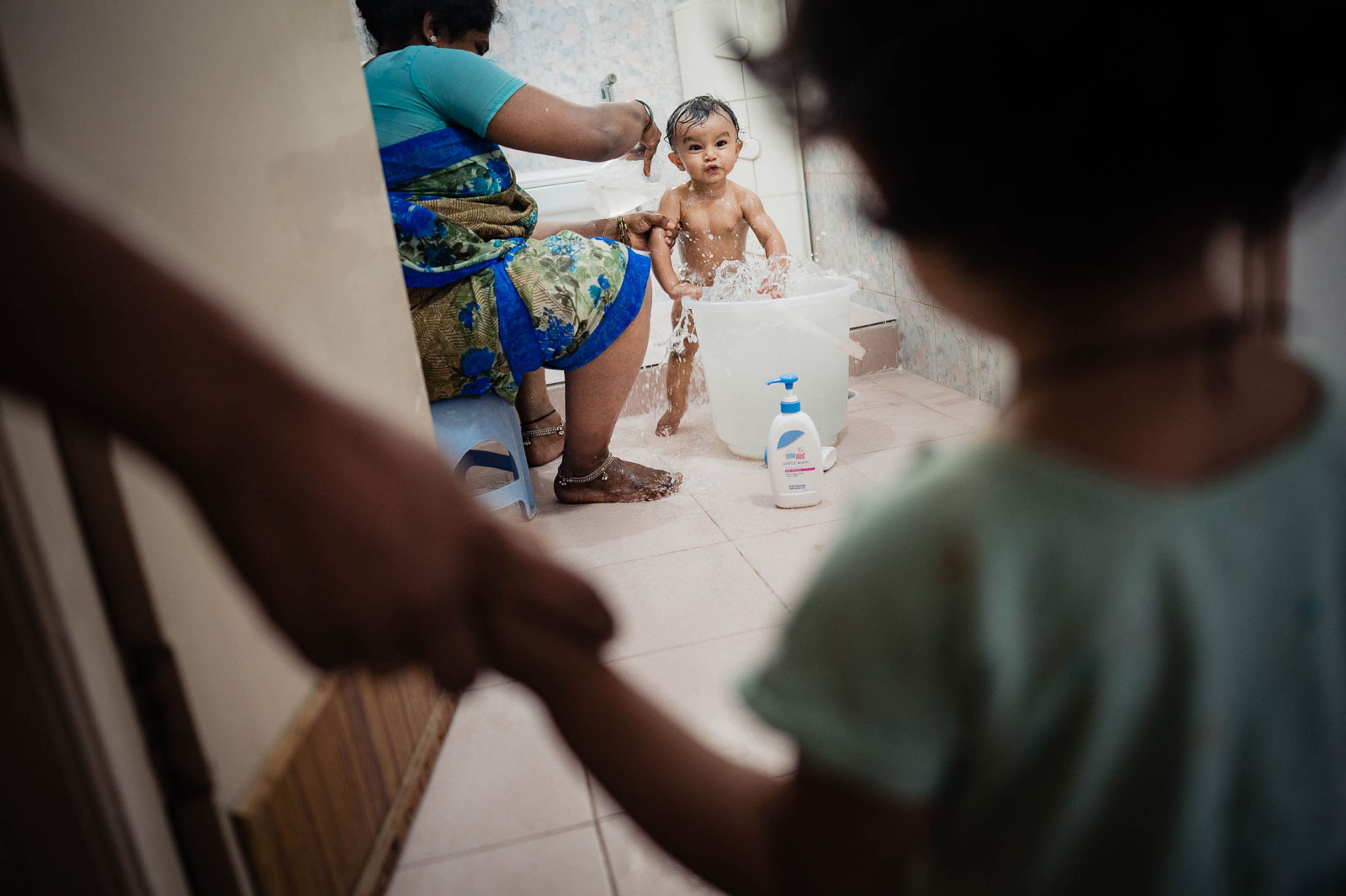 Adult bathing a young child in a tiled bathroom with soap and water